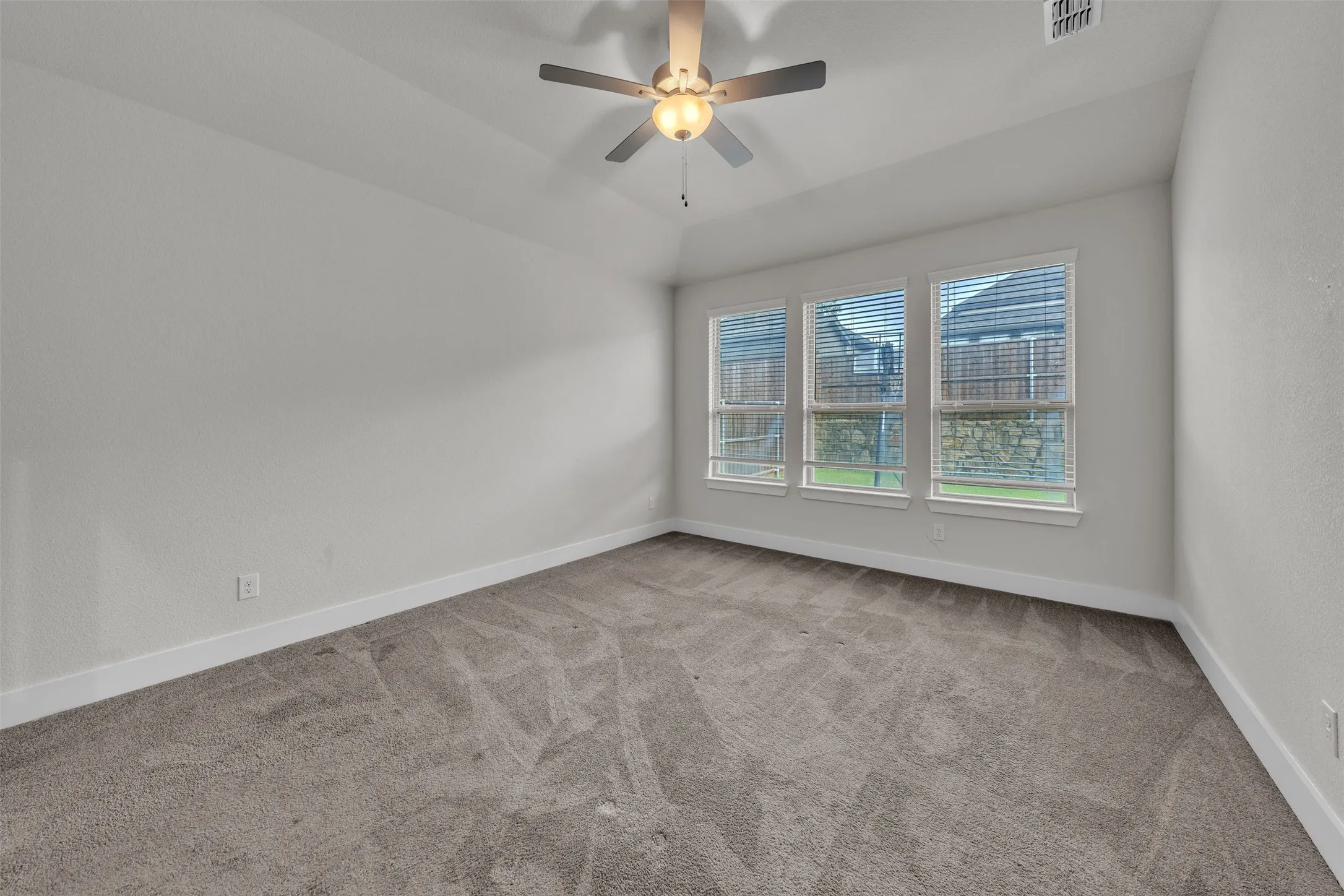 Primary Bedroom at 5149 Cantle Ct in Fort Worth, Texas, Tarrant County, with light colored carpet and three large windows looking into the backyard. Ceiling fan with dual switch. Located on first floor away from all other bedrooms.