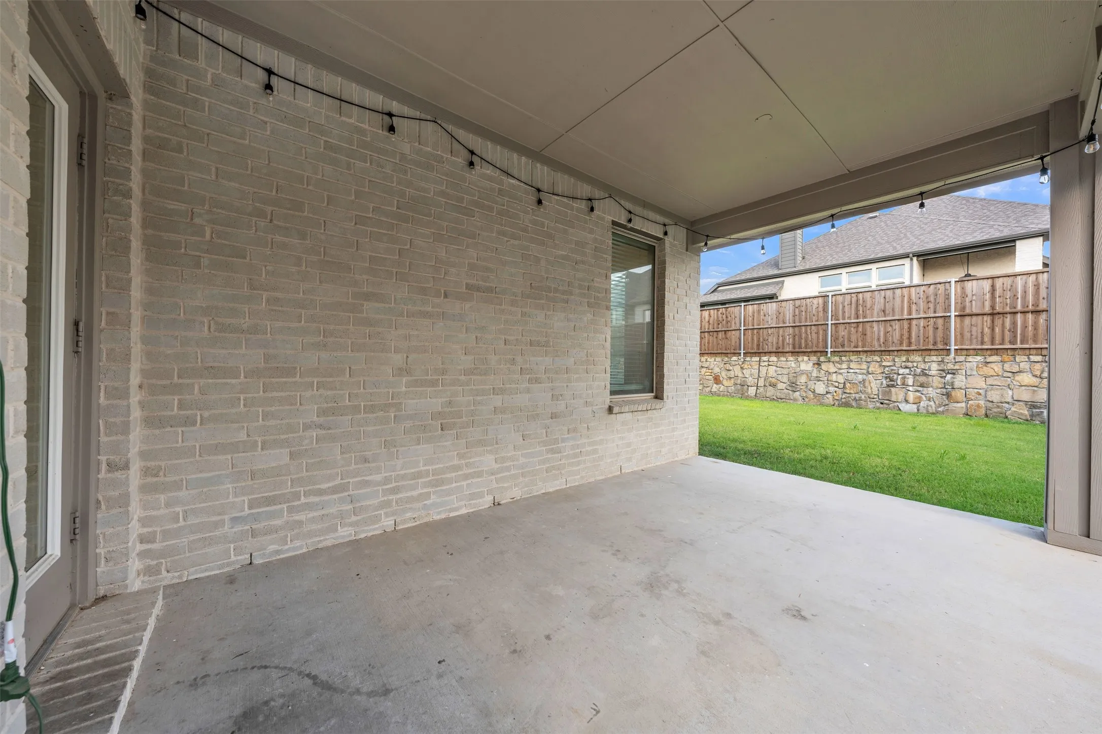 Covered Patio at 5149 Cantle Ct in Fort Worth, Texas, Tarrant County, overlooking backyard with rock retaining wall and wooden privacy fence.