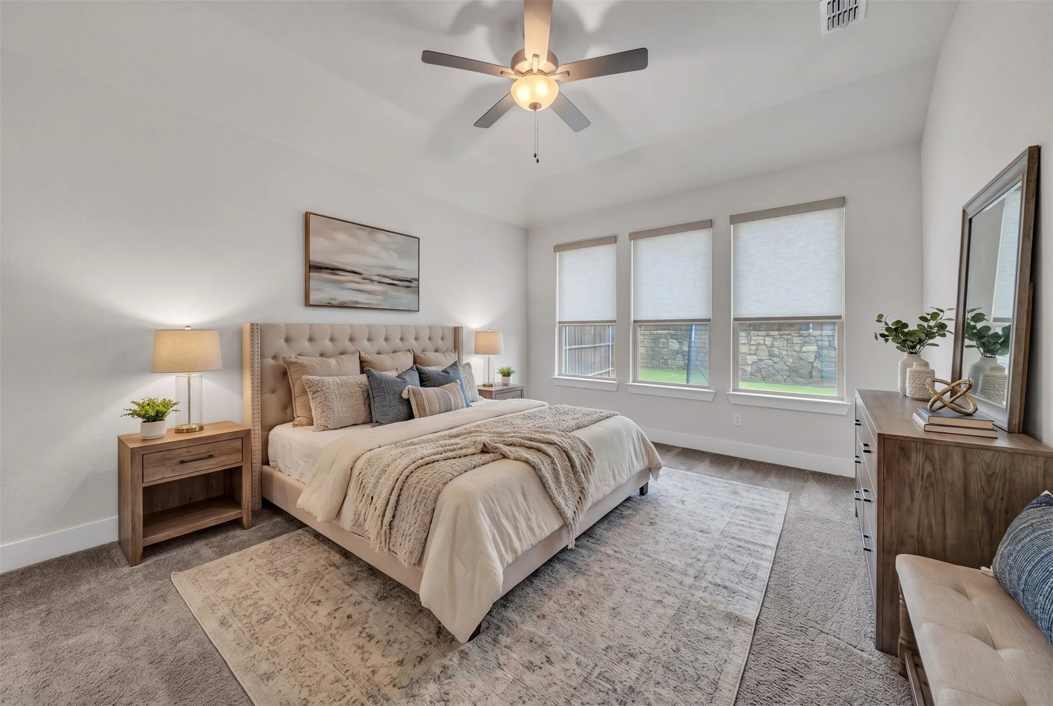 Virtually Staged Primary Bedroom at 5149 Cantle Ct in Fort Worth, Texas, Tarrant County, with light colored carpet and three large windows looking into the backyard. Ceiling fan with dual switch. Located on first floor away from all other bedrooms.