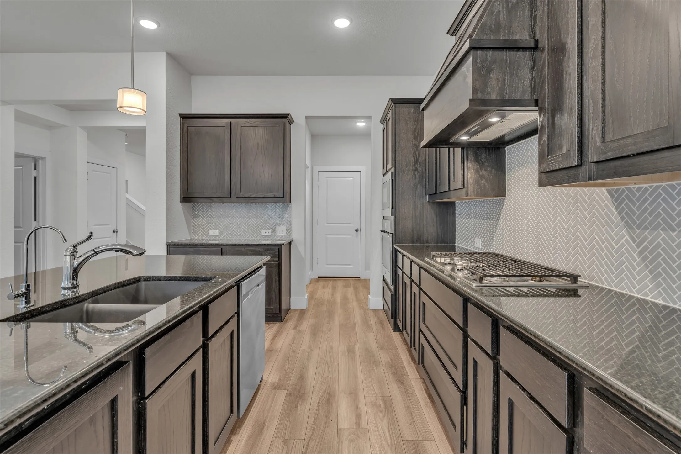 Kitchen at 5149 Cantle Ct in Fort Worth, Texas, Tarrant County, with large kitchen island, brown wooden cabinets, neutral herringbone backsplash, and separate cooktop.