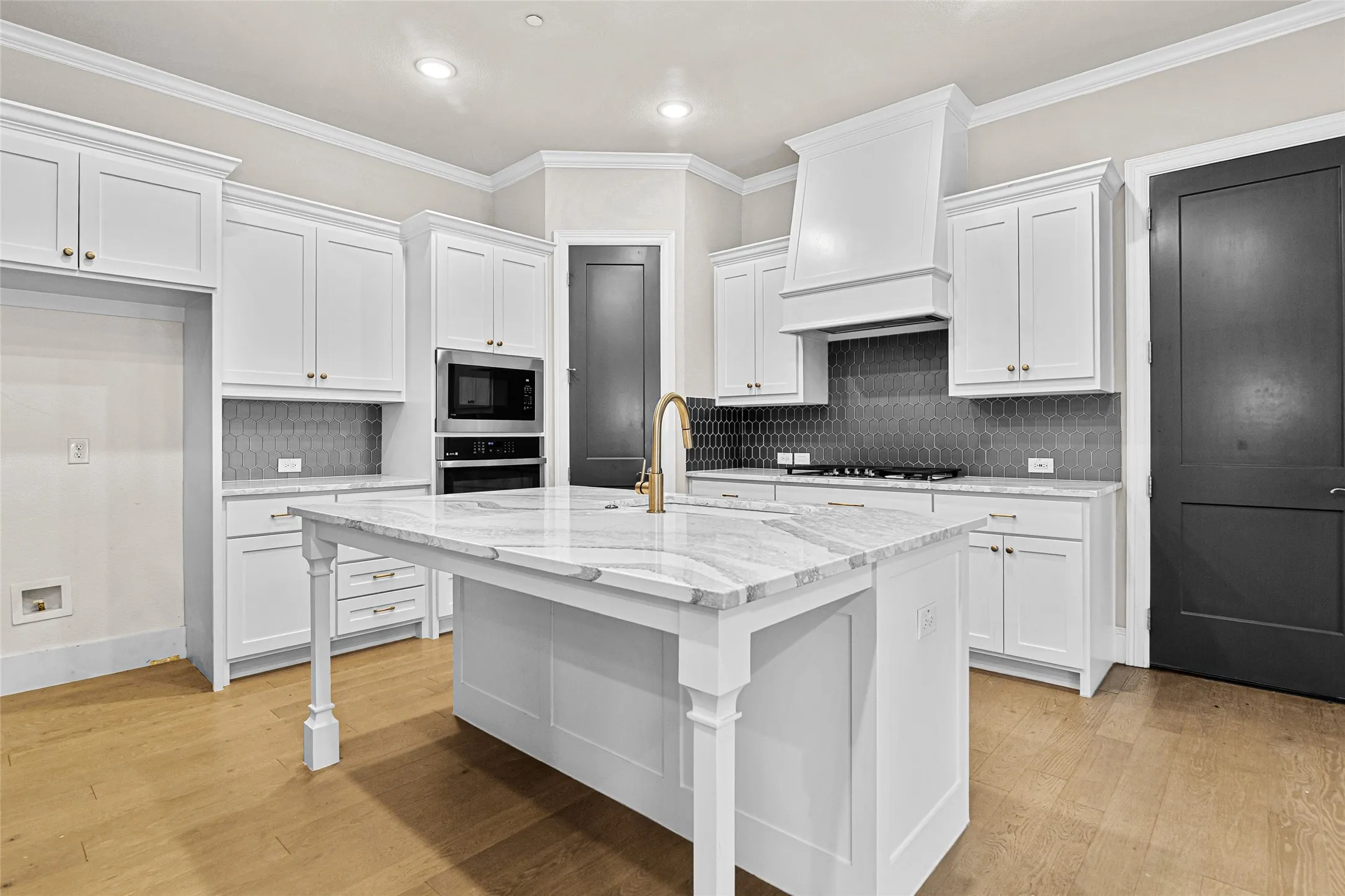 Gourmet kitchen featuring a substantial island with a patterned countertop, white cabinetry, integrated stainless steel appliances, a gray hexagonal tile backsplash, and wood-finish flooring