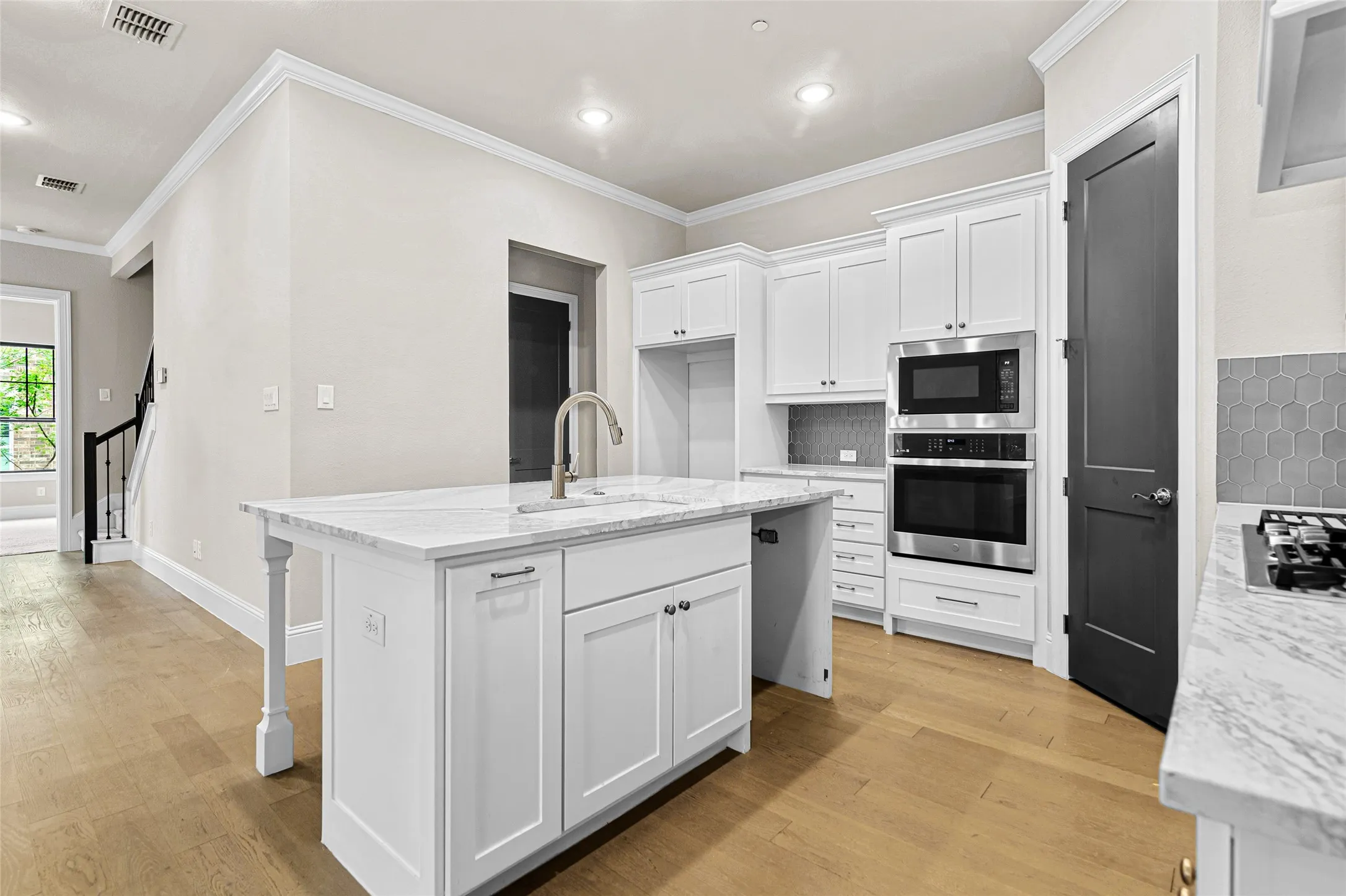 Open-concept kitchen featuring a central island with an undermount sink, white cabinetry, stainless steel appliances, marble-look countertops, and wood-finish flooring