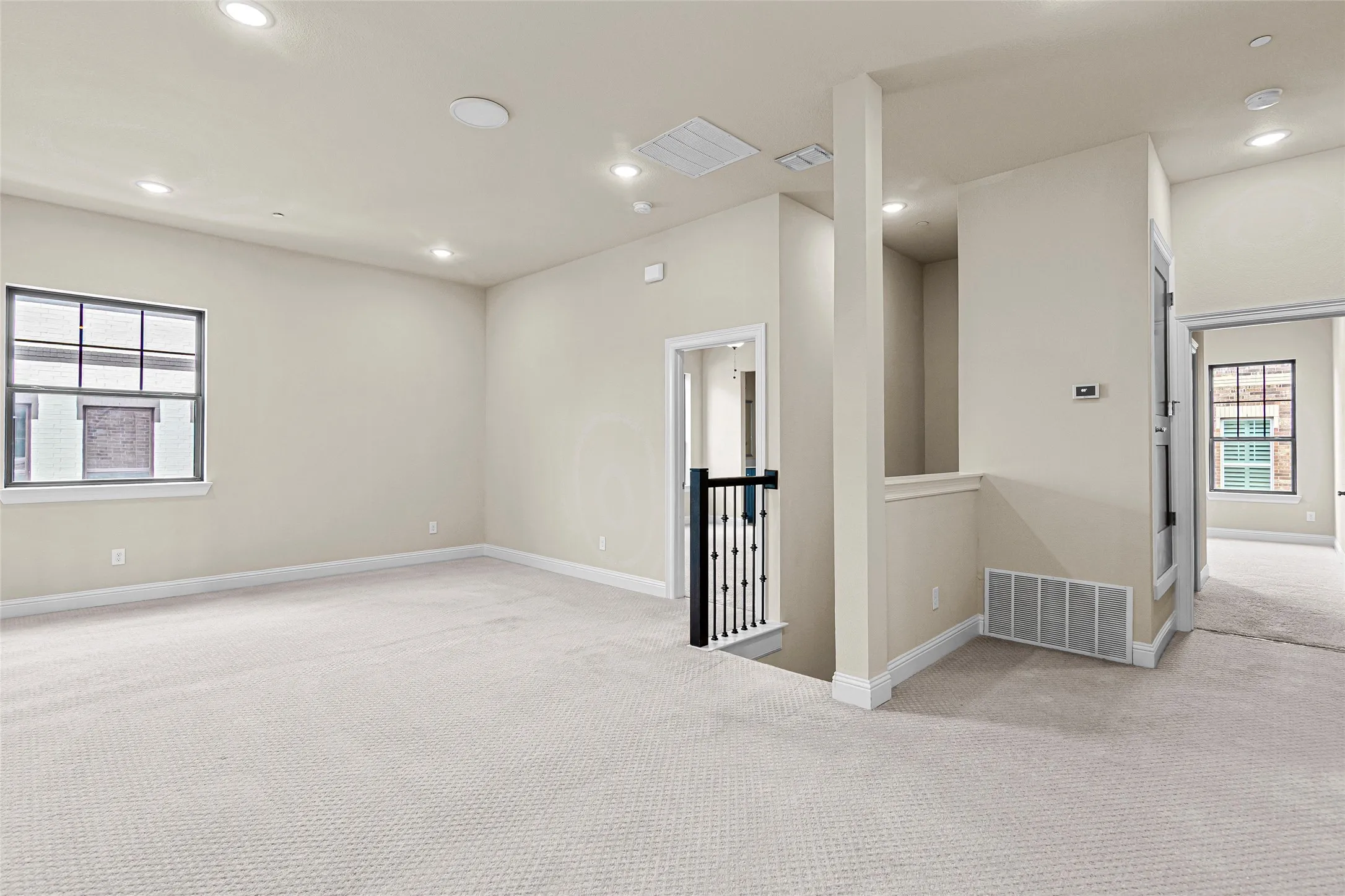 Spacious carpeted room featuring recessed lighting, a multi-pane window, and a painted baluster railing