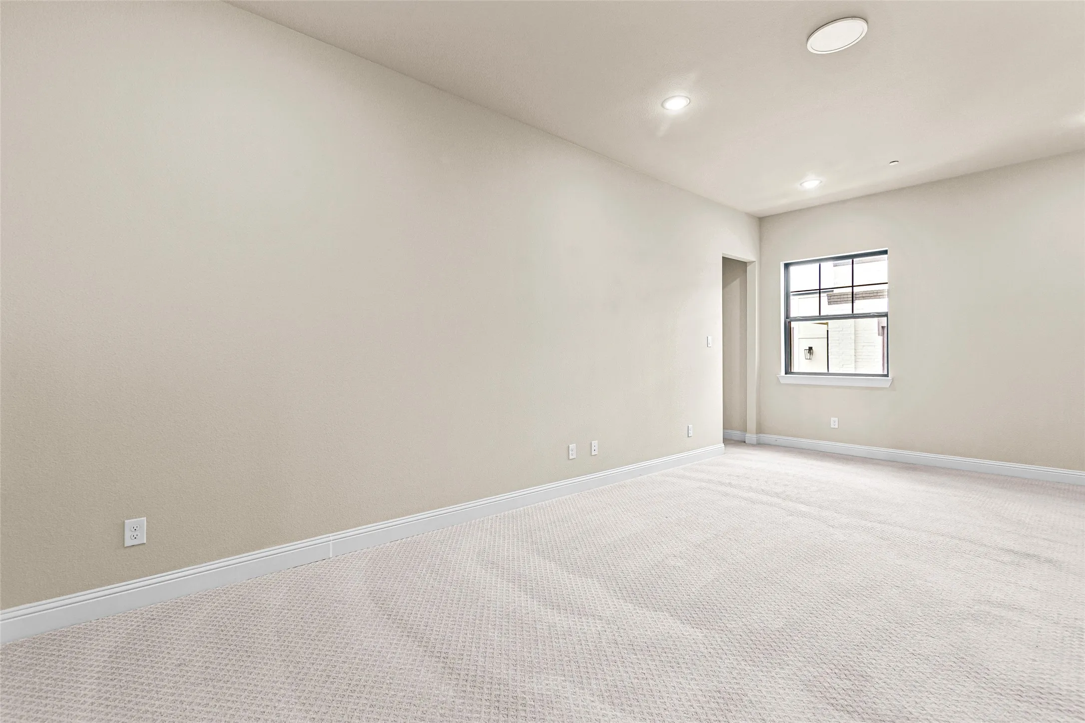 Upstairs living room is spacious.  Featuring neutral carpeting, light-toned walls, and a large window with dark trim.