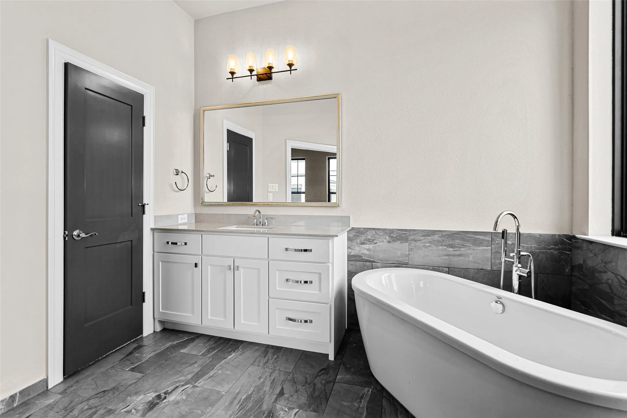 2nd floor primary Bathroom. Bathroom featuring a freestanding soaking tub with floor-mounted chrome hardware, a white vanity with a light-toned countertop, a rectangular framed mirror, and a four-light fixture