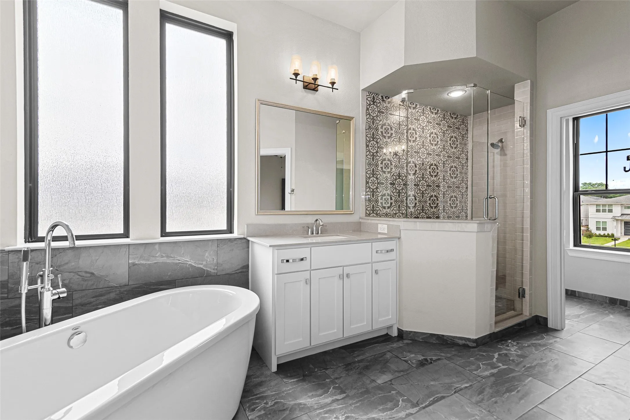 2nd floor primary Bathroom. Freestanding soaking tub with a floor-mounted chrome faucet, dual vanity with shaker-style cabinetry and a stone-finish countertop, and a walk-in shower featuring decorative tile and a glass enclosure