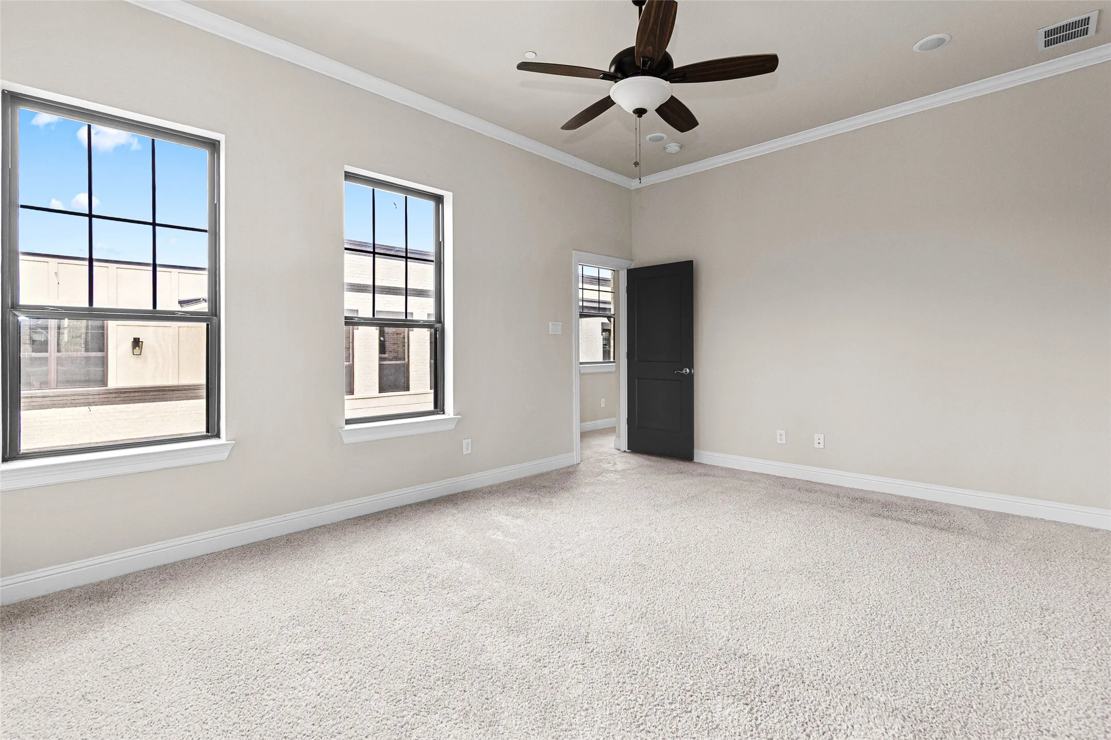 Spacious primary bedroom featuring light-colored carpeting, two large windows with grid patterns, a ceiling fan with integrated lighting, recessed ceiling lighting, and crown molding
