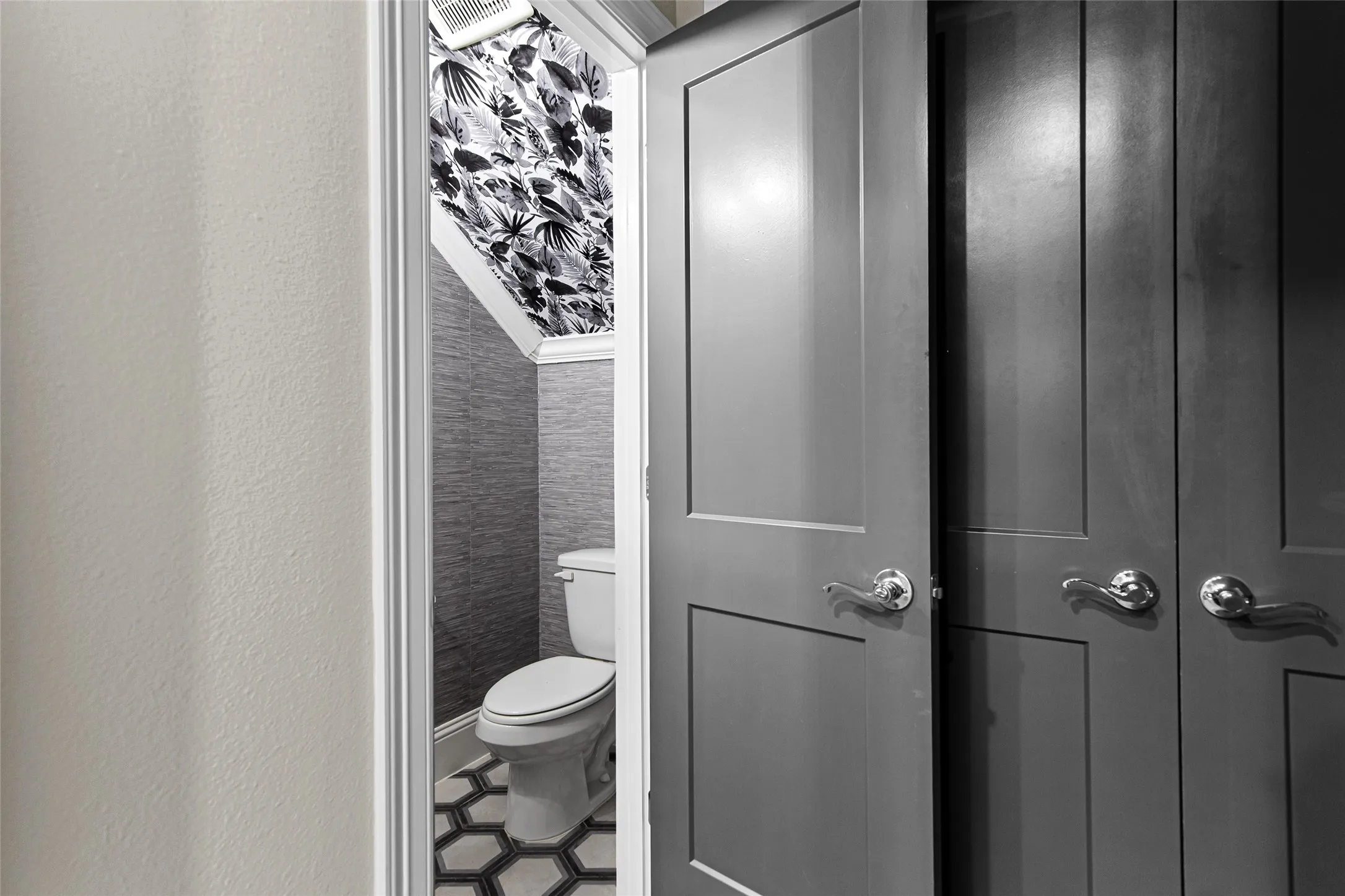 Powder room featuring a white toilet, hexagonal floor tiling, and dark patterned wallpaper.
Half bathroom is located on the first floor.