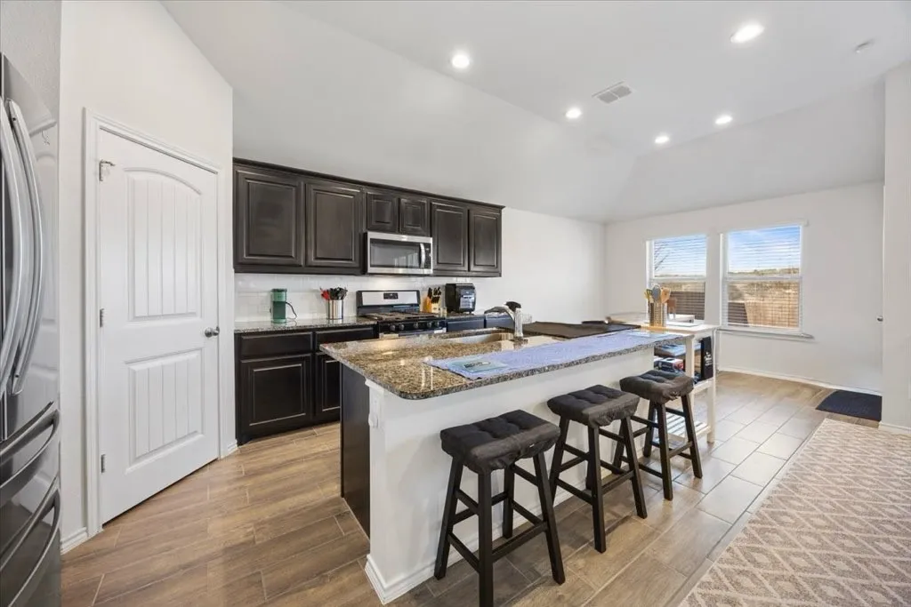 Kitchen featuring dark wood cabinetry, a granite-topped island with seating, a tile backsplash, and wood-finish flooring