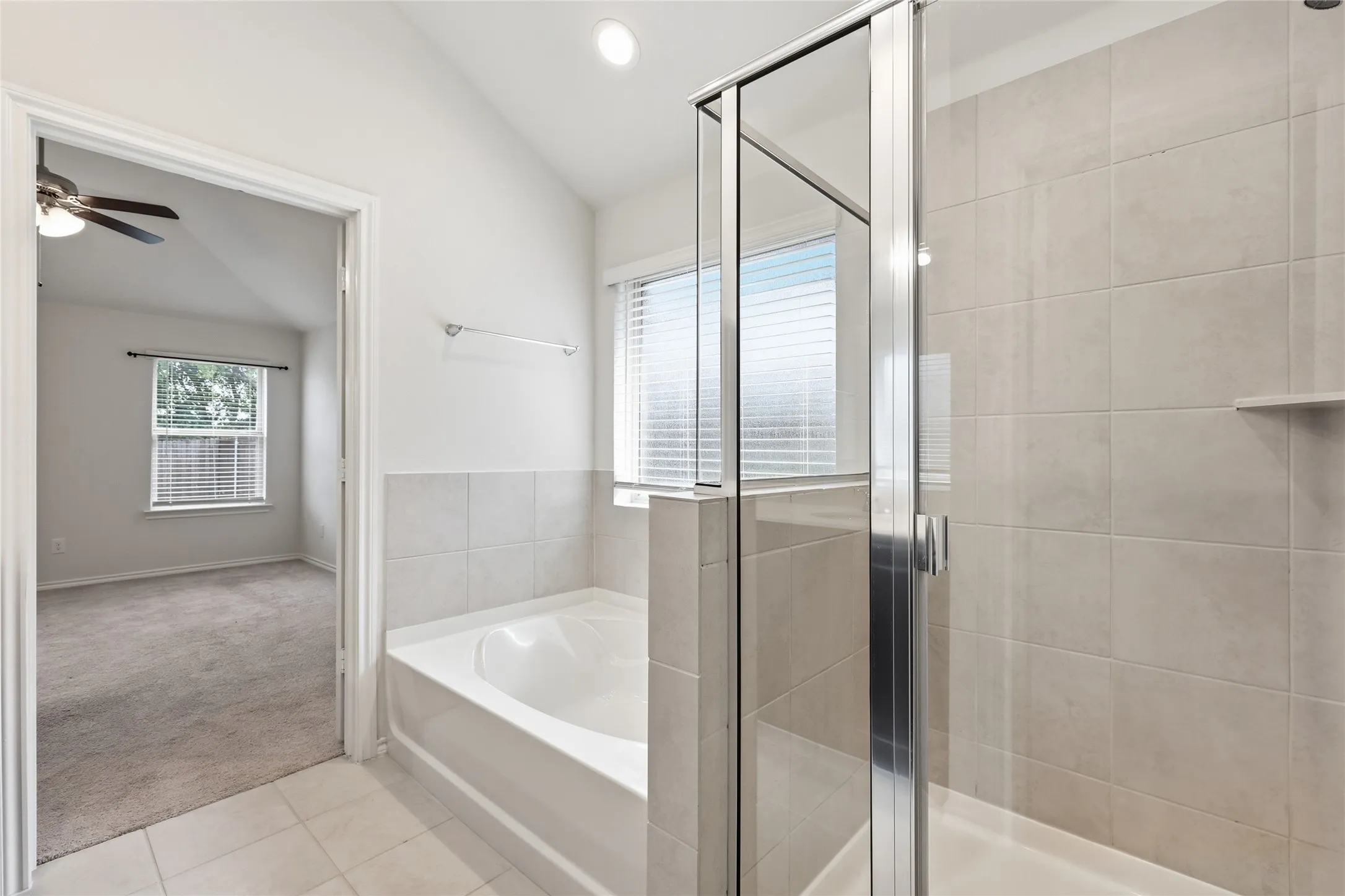Bathroom featuring a built-in tub, separate glass-enclosed shower, light-toned tile flooring, and matching tiled shower surround