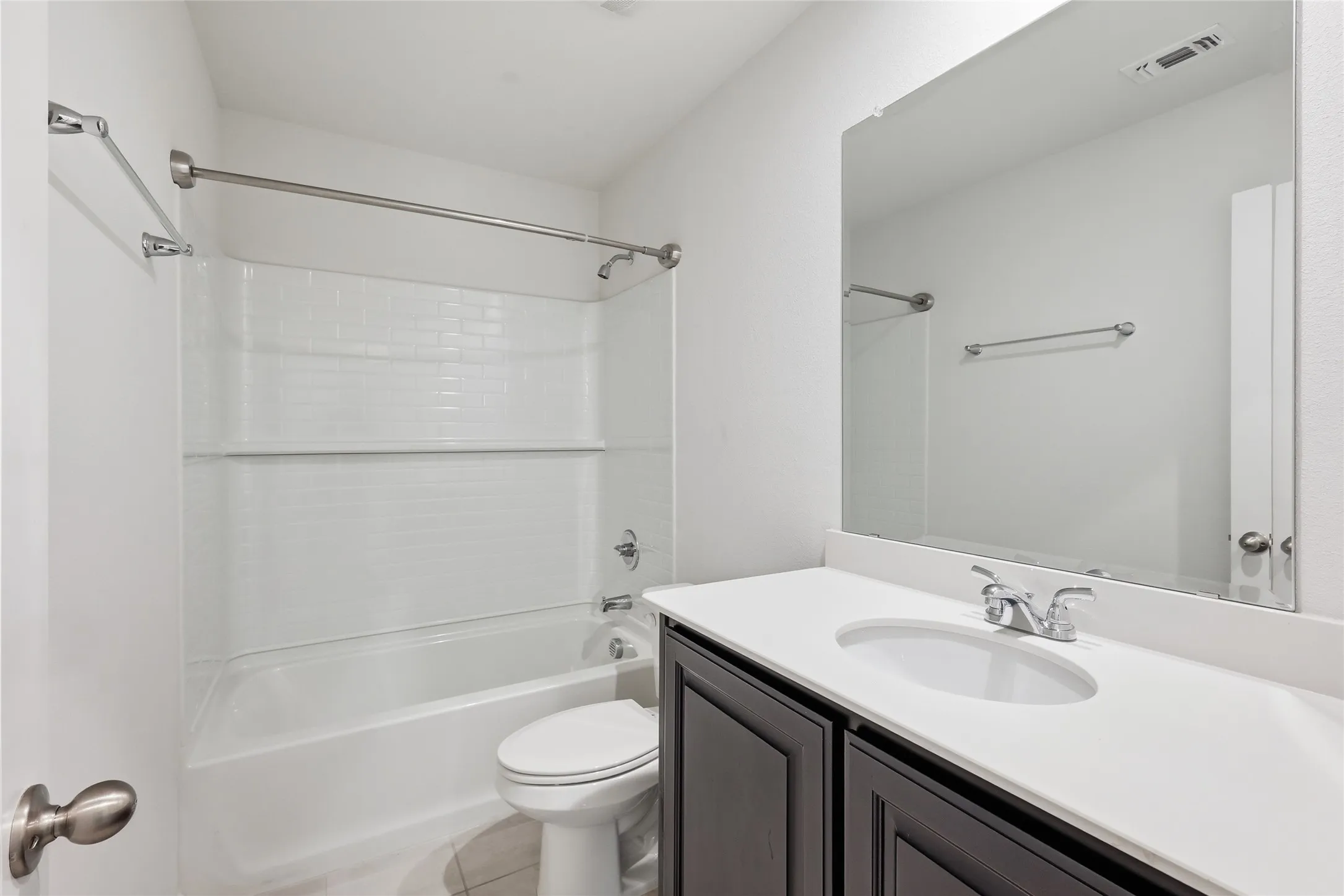 Bathroom featuring a white bathtub with subway tile surround, dark wood-finish vanity with an integrated sink, polished chrome faucet, and a large wall-mounted mirror
