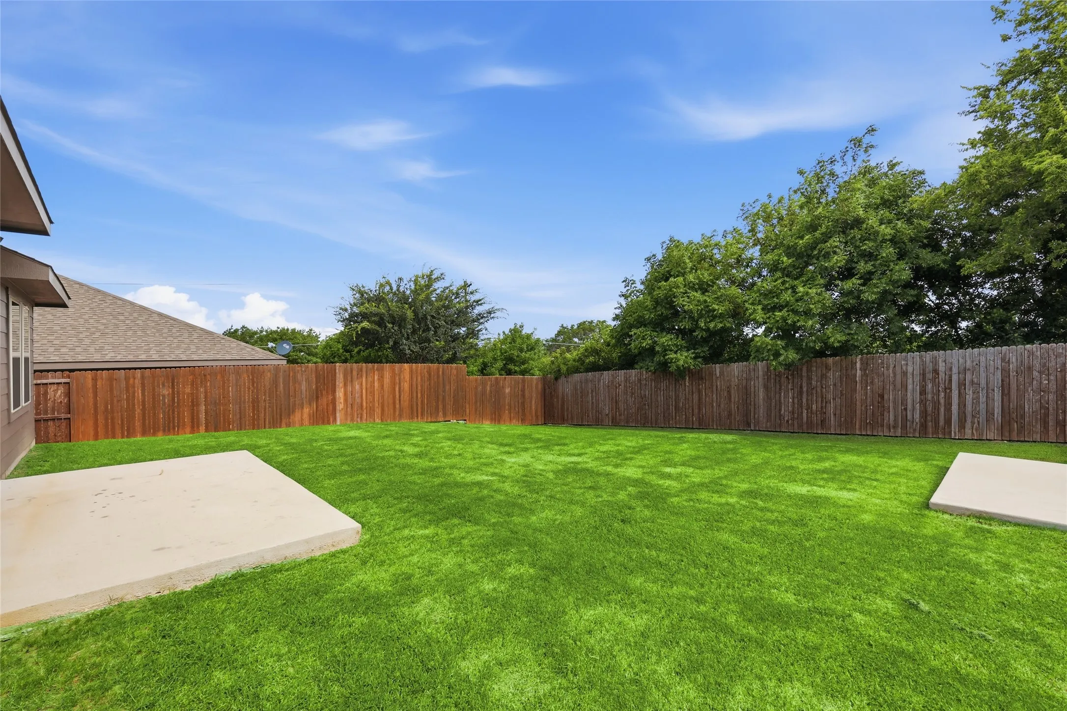Expansive rear yard featuring green lawn, a tall wooden privacy fence, and two concrete pad areas