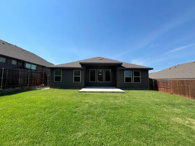 Expansive rear yard featuring a manicured lawn, dark siding, and a concrete patio