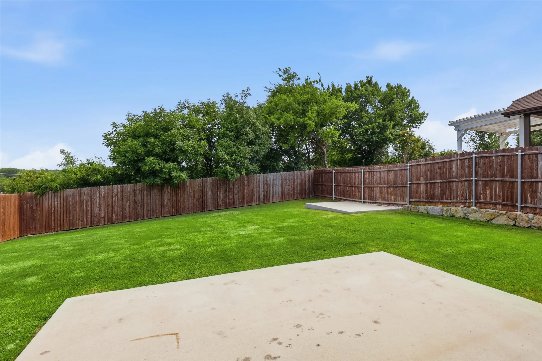 Expansive backyard featuring a lush lawn, privacy fencing, two concrete patios, and mature trees