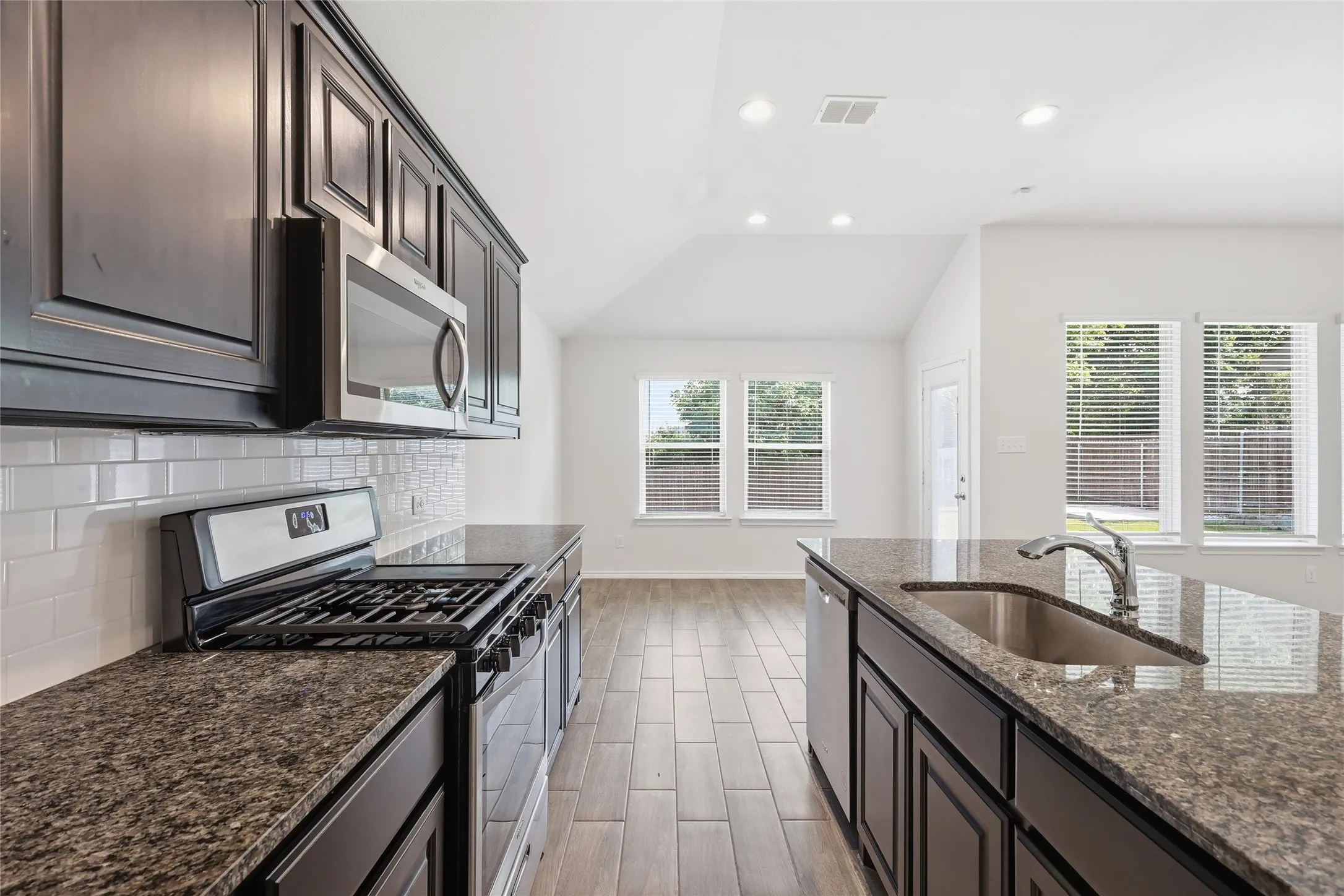Kitchen featuring dark cabinetry, speckled countertops, stainless steel appliances, white subway tile backsplash, and wood-finish flooring, gas range