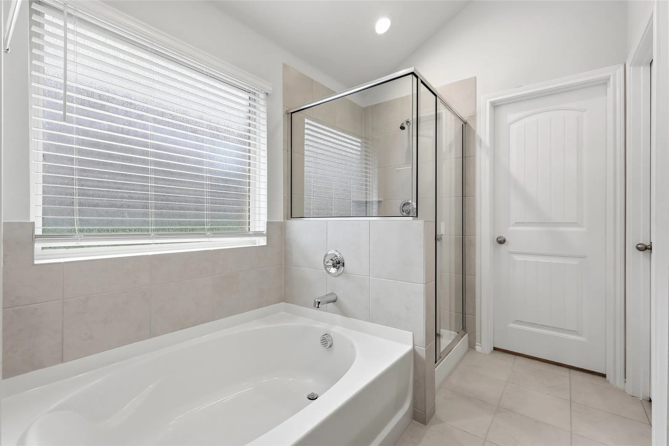 White soaking tub with chrome fixtures, glass-enclosed shower, tile flooring, and white paneled doors