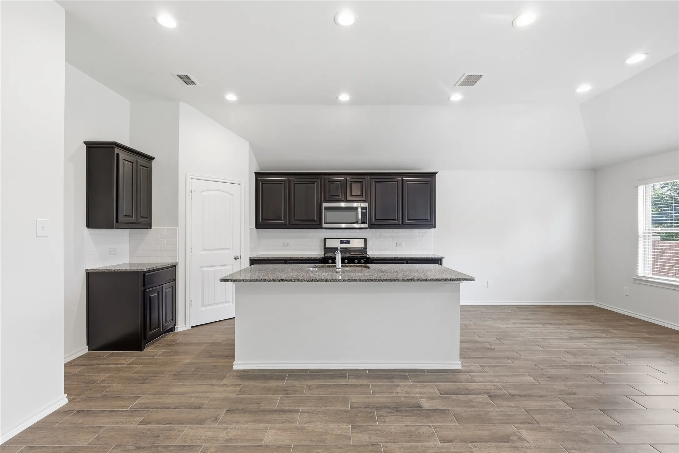 Open-concept kitchen featuring an island, dark wood cabinetry, stainless steel microwave, and white subway tile backsplash