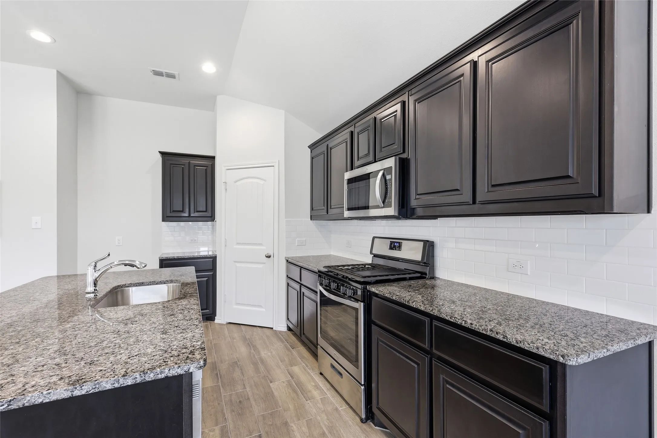 Kitchen featuring dark wood-finish cabinetry, granite countertops, subway tile backsplash, and stainless steel appliances