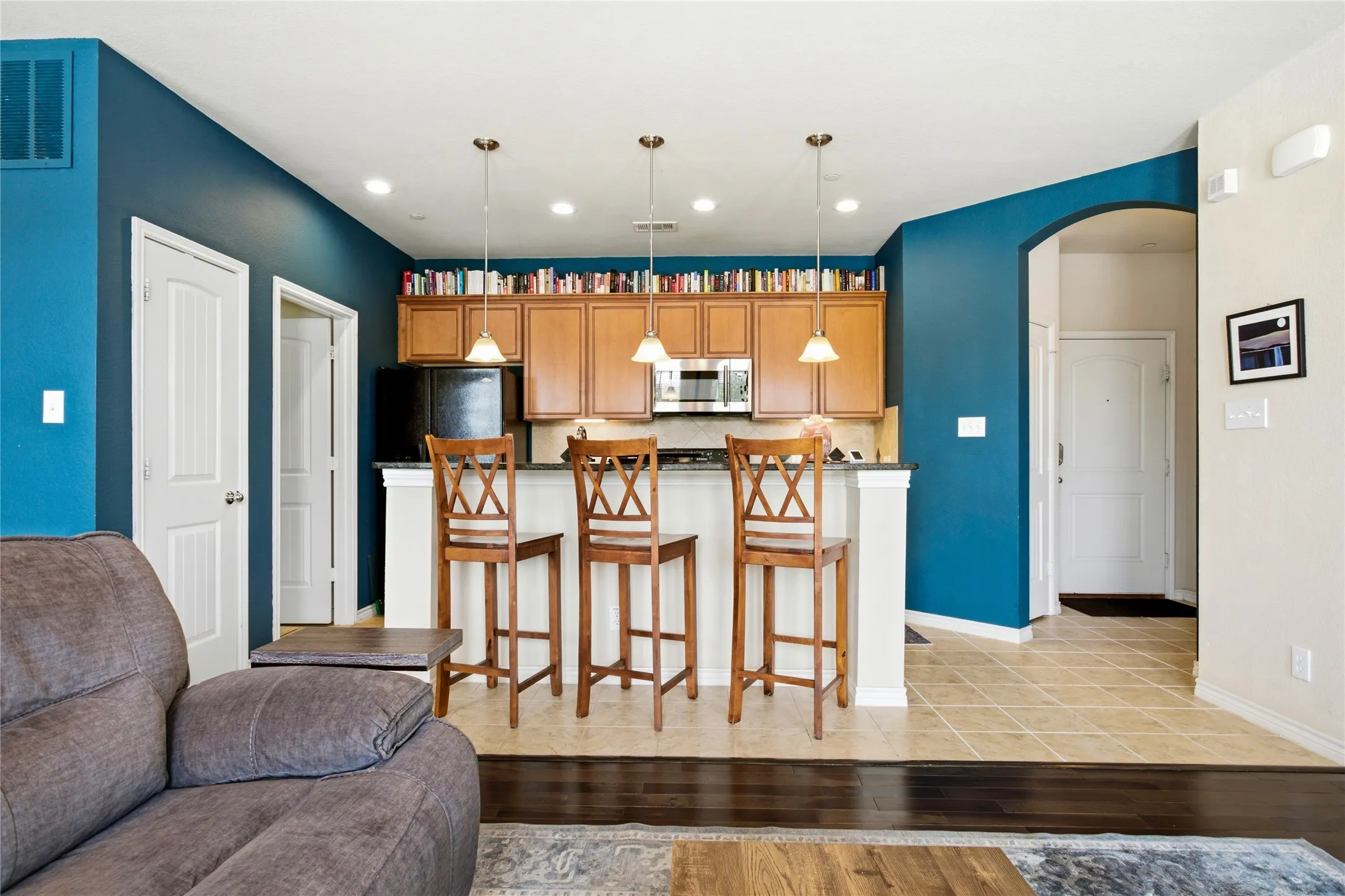 Kitchen with wood cabinetry, stainless steel appliances, and island with pendant lighting - barstools included.