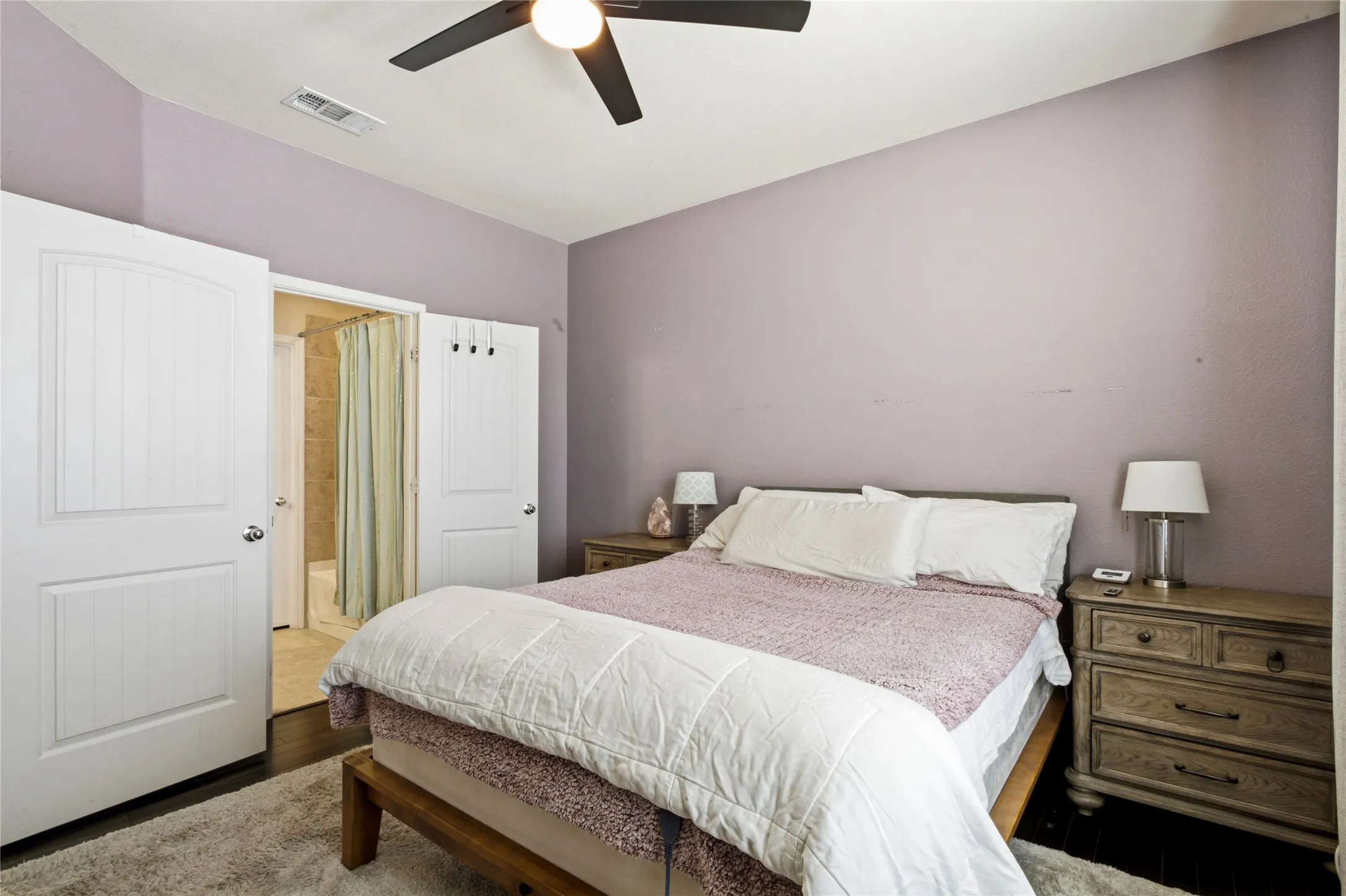 Bedroom featuring a ceiling fan with integrated lighting, wood-finish flooring, and a private bath with a tiled shower