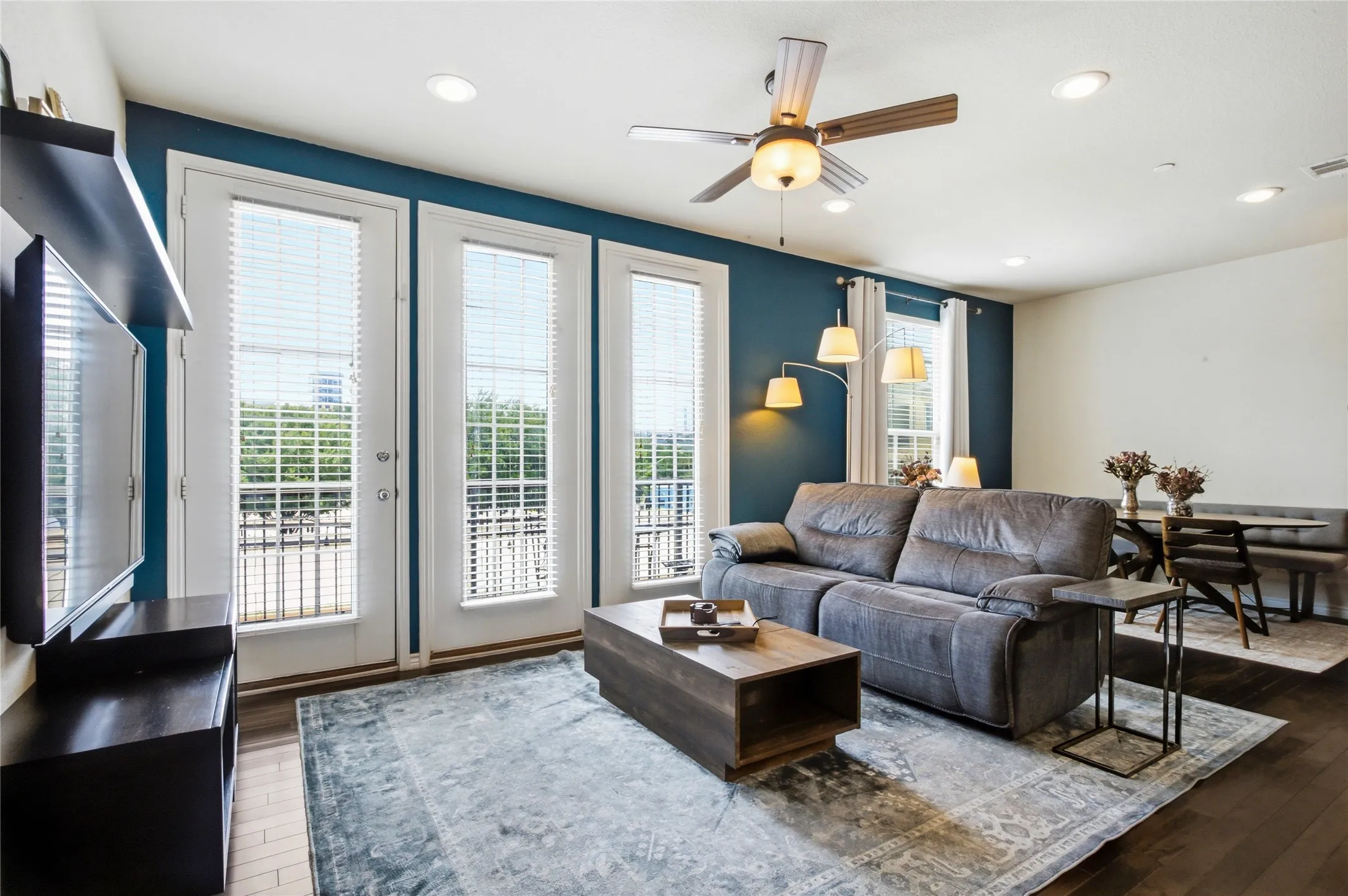 Beautiful windows and a patio make it a great space to watch the sunset. Living is an open-concept living area featuring dark wood-finish flooring, recessed lighting, and a ceiling fan.