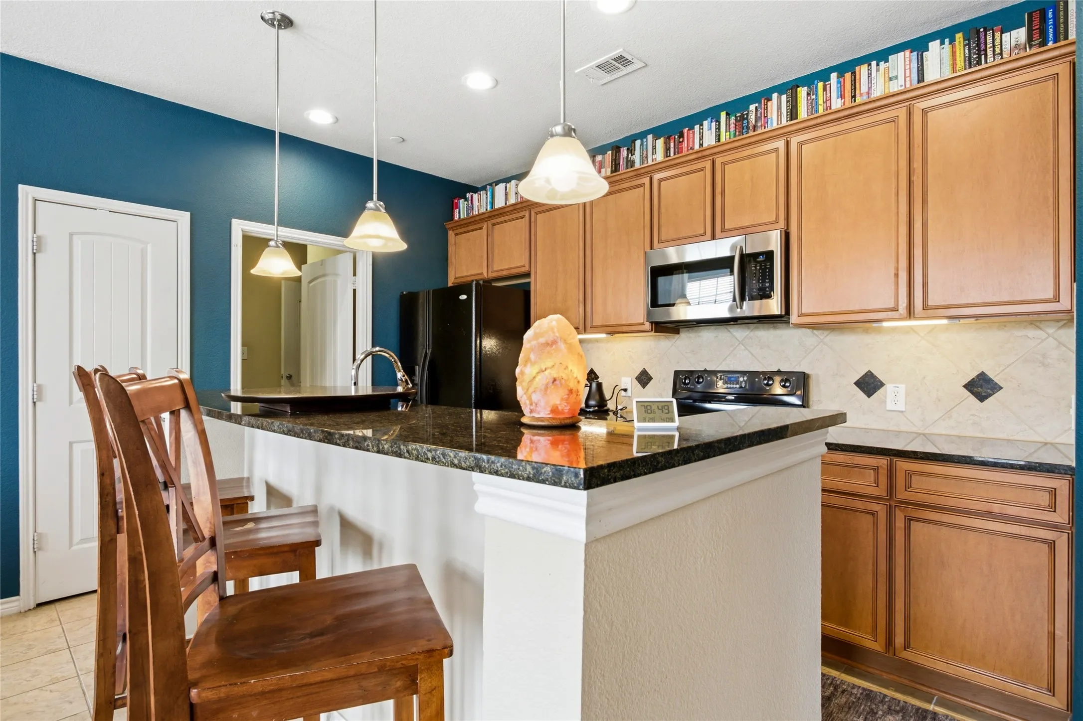 Kitchen featuring a breakfast bar with stone-finish countertop, pendant lighting, stainless steel microwave, and wood-finish cabinetry