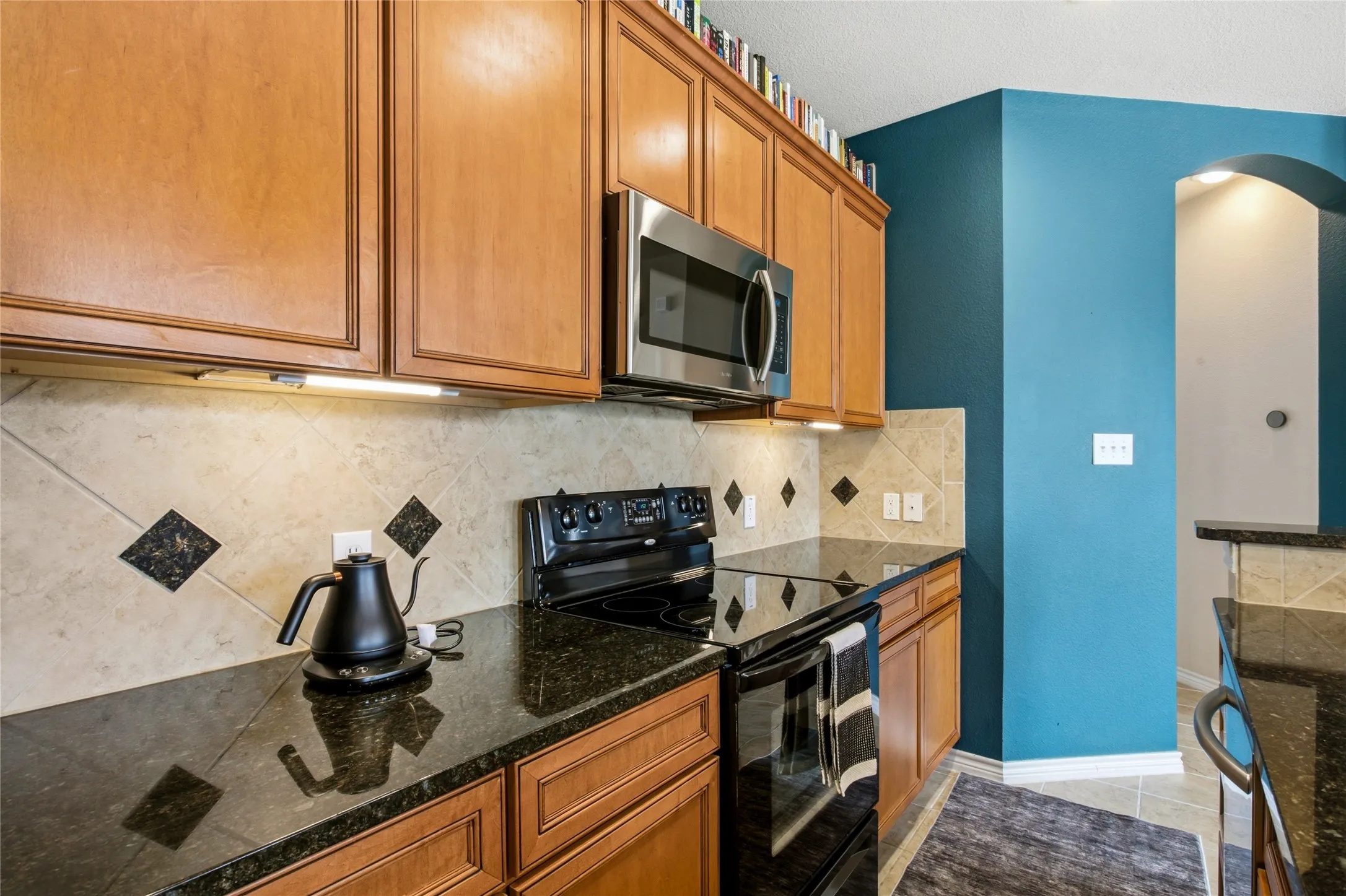 Kitchen featuring wood cabinetry, stainless steel microwave, black electric range, and dark countertops