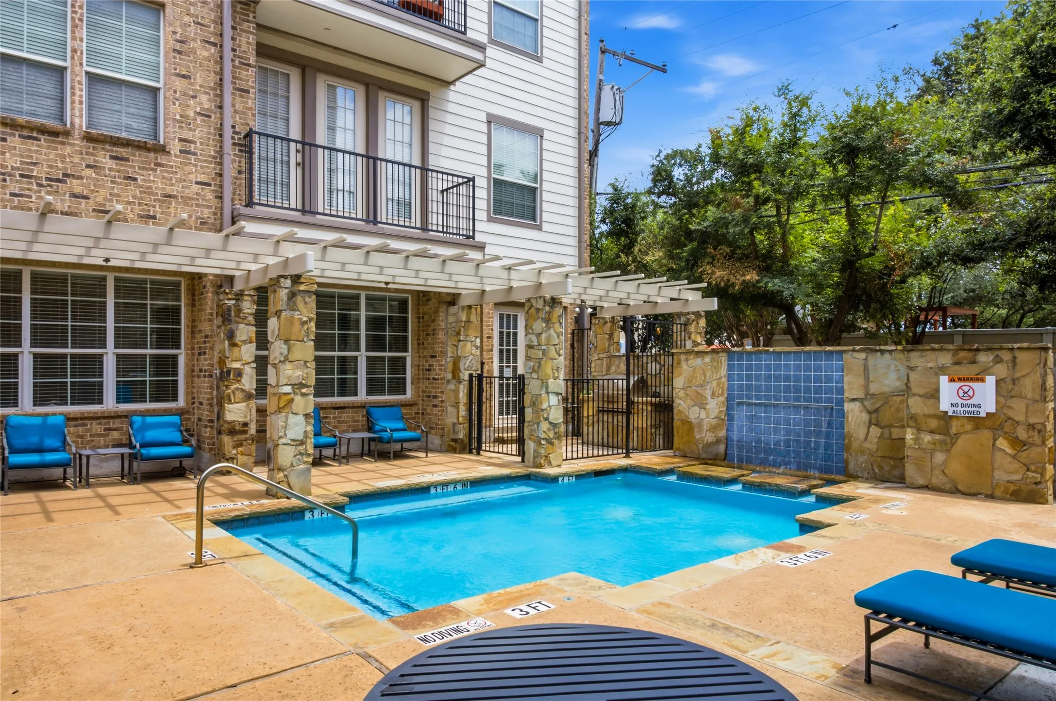 Outdoor swimming pool with a stone tile surround, integrated water feature, and a pergola-covered patio area