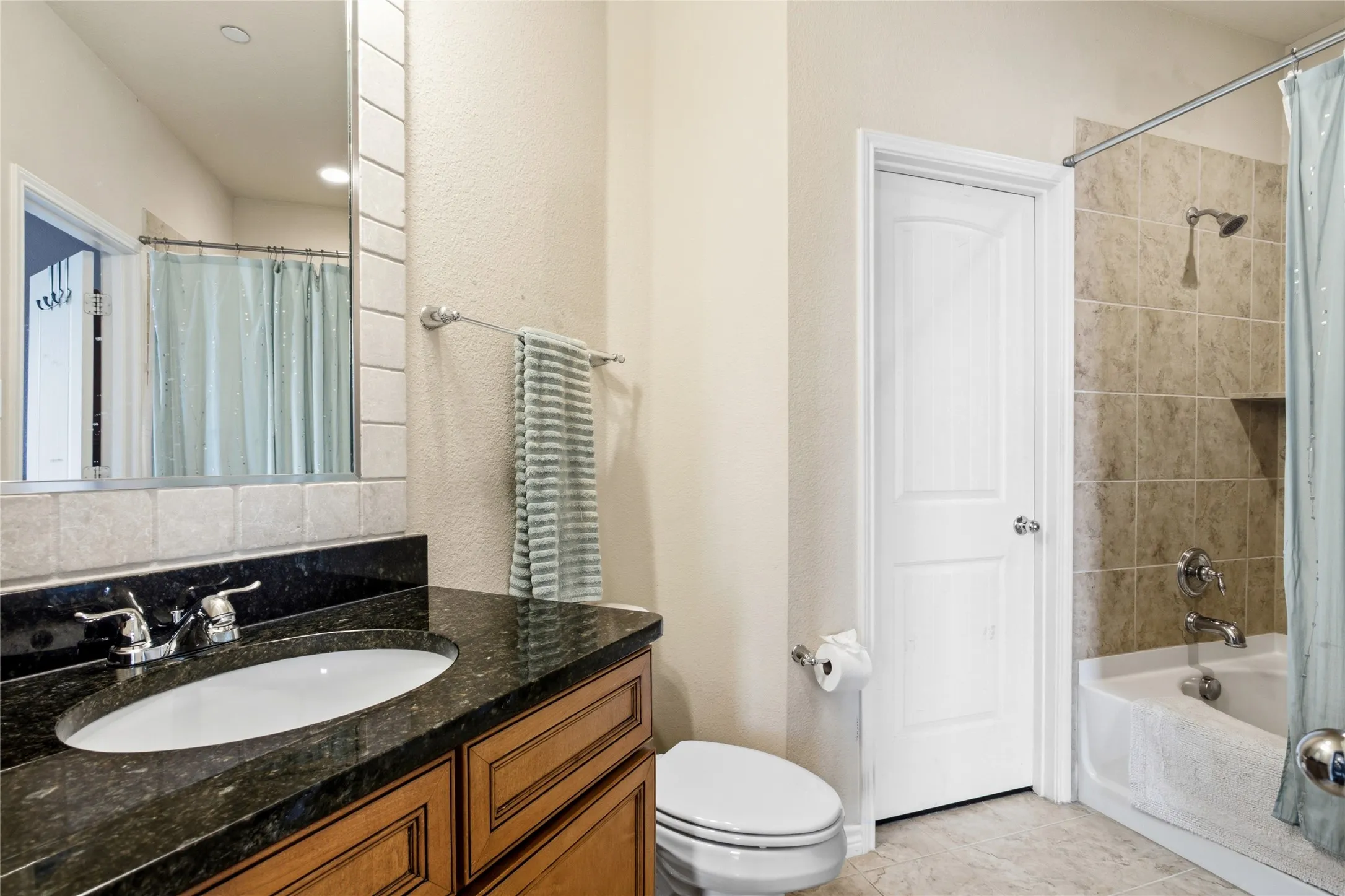 Bathroom featuring a dark stone-finish vanity countertop, an undermount sink with a chrome faucet, and a light wood-finish cabinet