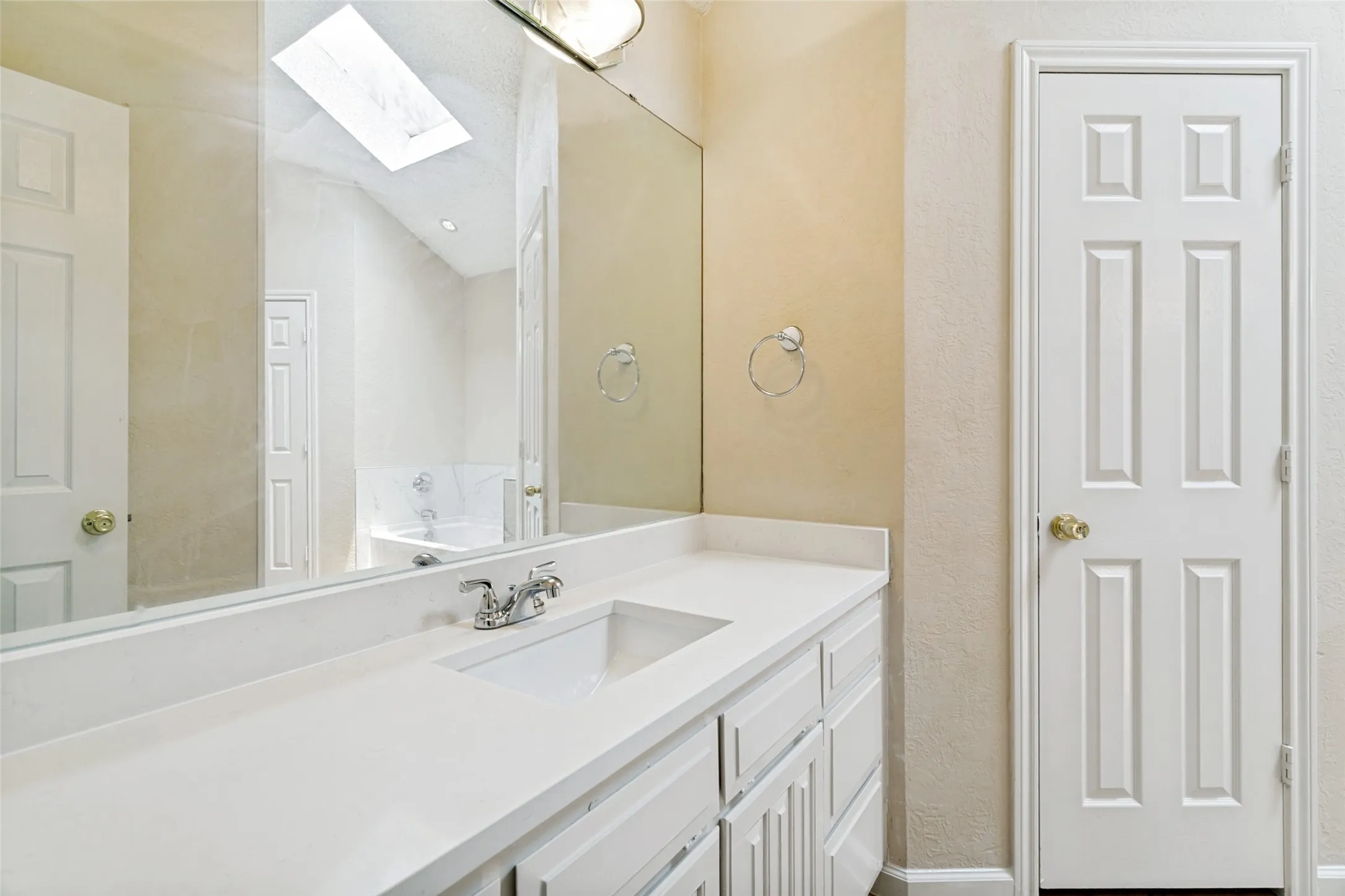 Vanity featuring a white countertop with an integrated sink and chrome faucet, under-cabinet storage, and a large mirror