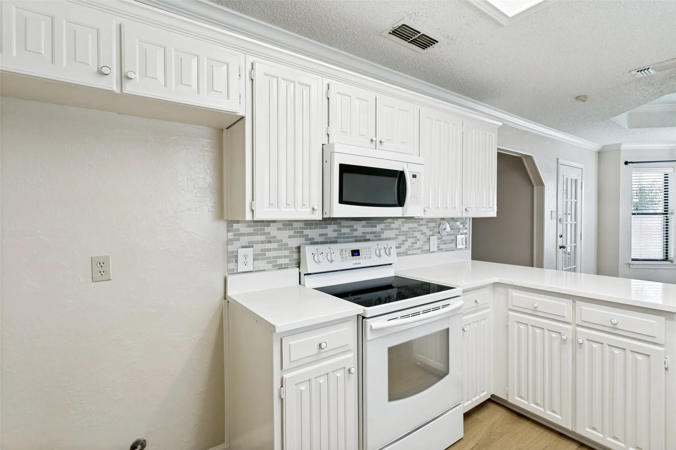 White kitchen featuring shaker-style cabinetry, a built-in microwave, an electric range, solid surface countertops, and a mosaic tile backsplash