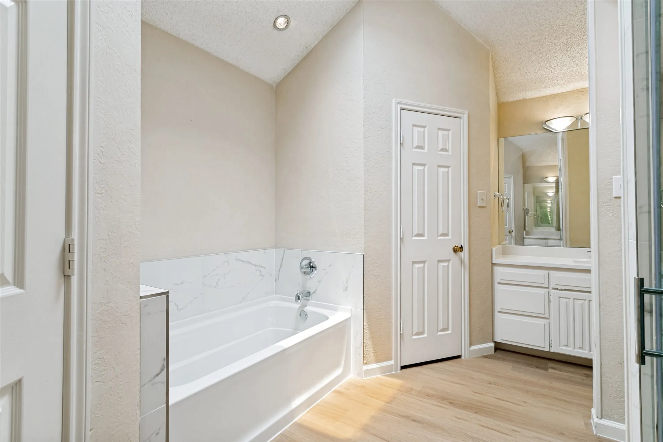 Bathtub with a white surround and a marble-look tile accent wall