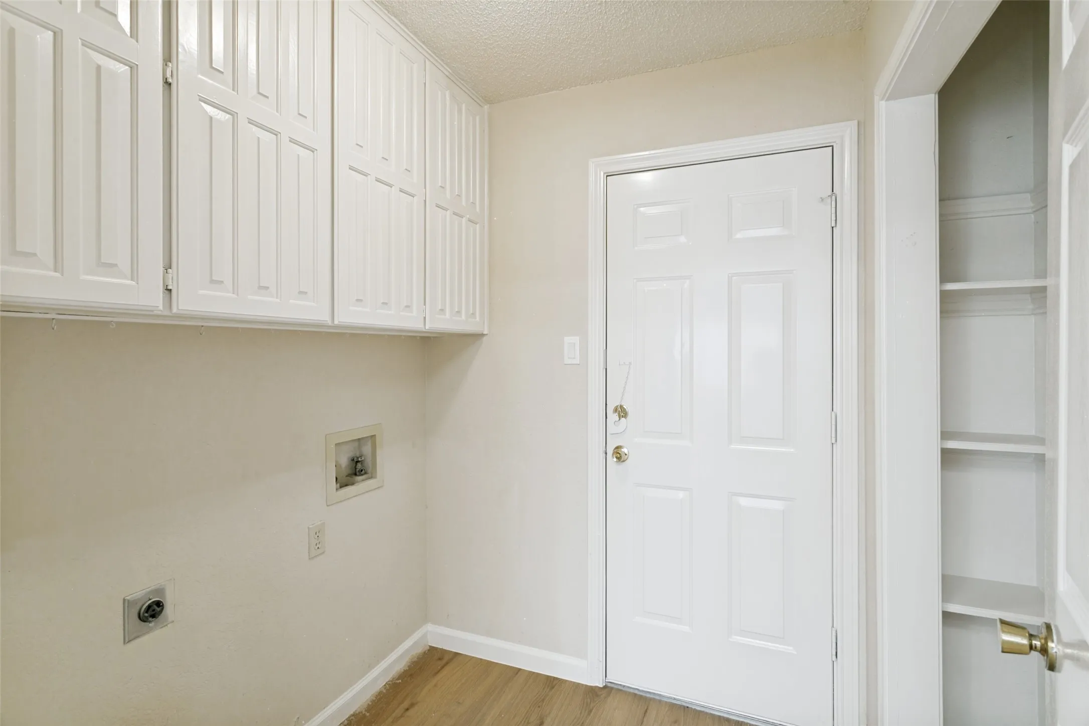 Utility space featuring white shaker-style cabinetry, wood-finish flooring, a paneled door, and built-in shelving