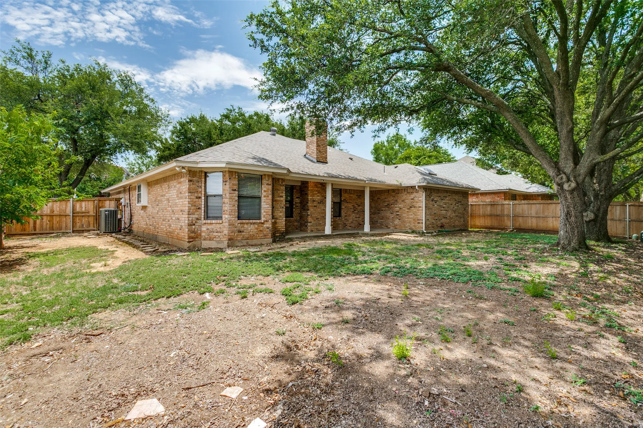 Expansive backyard with a brick exterior, covered patio, and mature trees