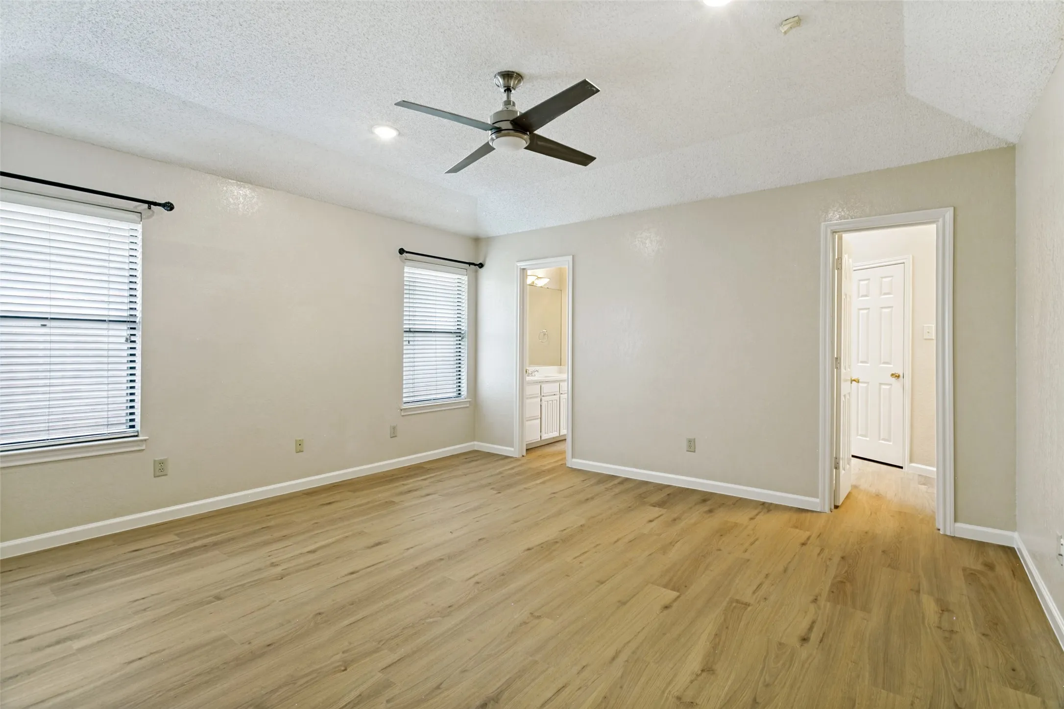 Spacious room featuring light wood-finish flooring, two windows with blinds, a ceiling fan, and recessed lighting