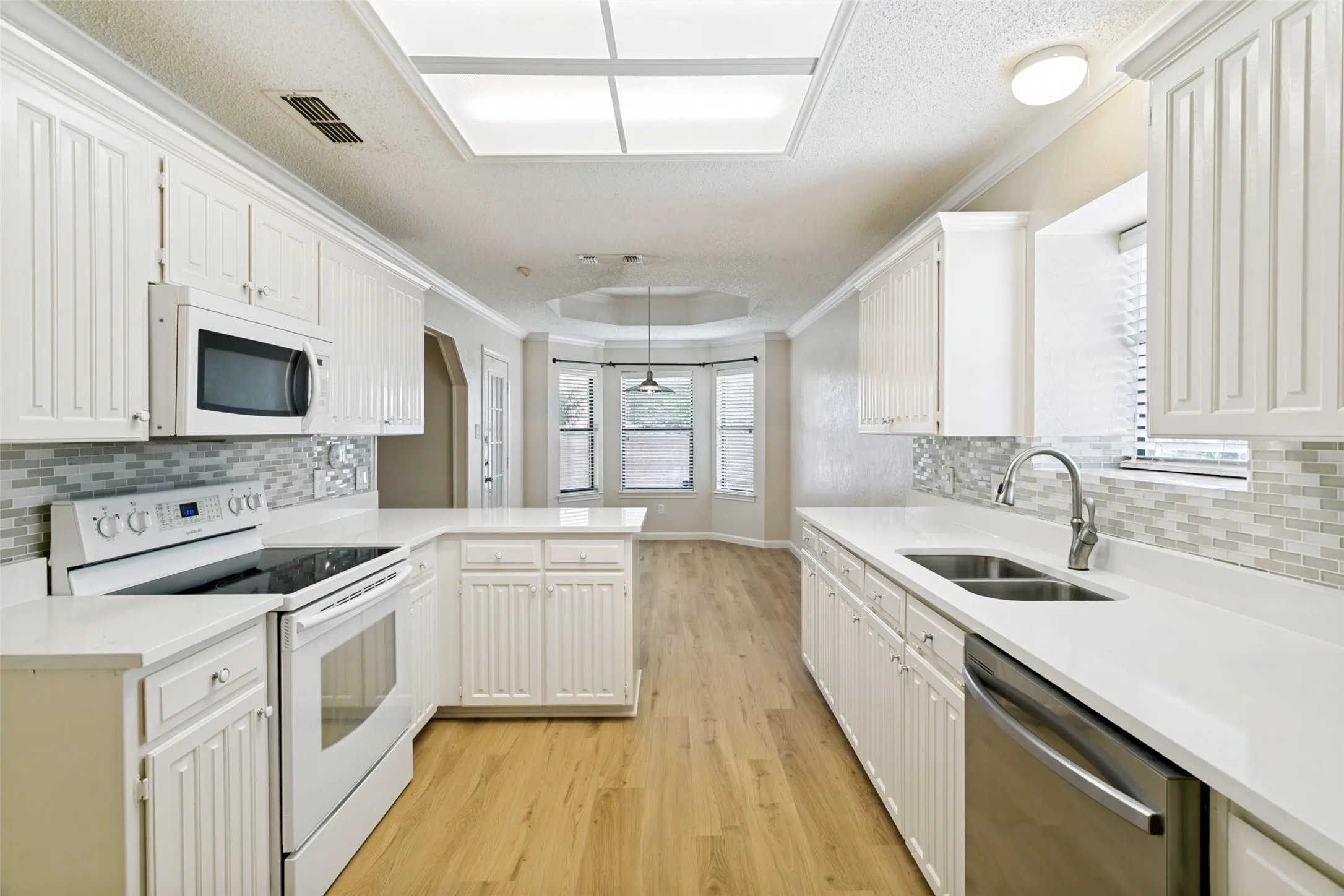Bright kitchen featuring wood-finish flooring, white cabinetry, integrated stainless steel dishwasher, and a glass-top electric range with microwave above
