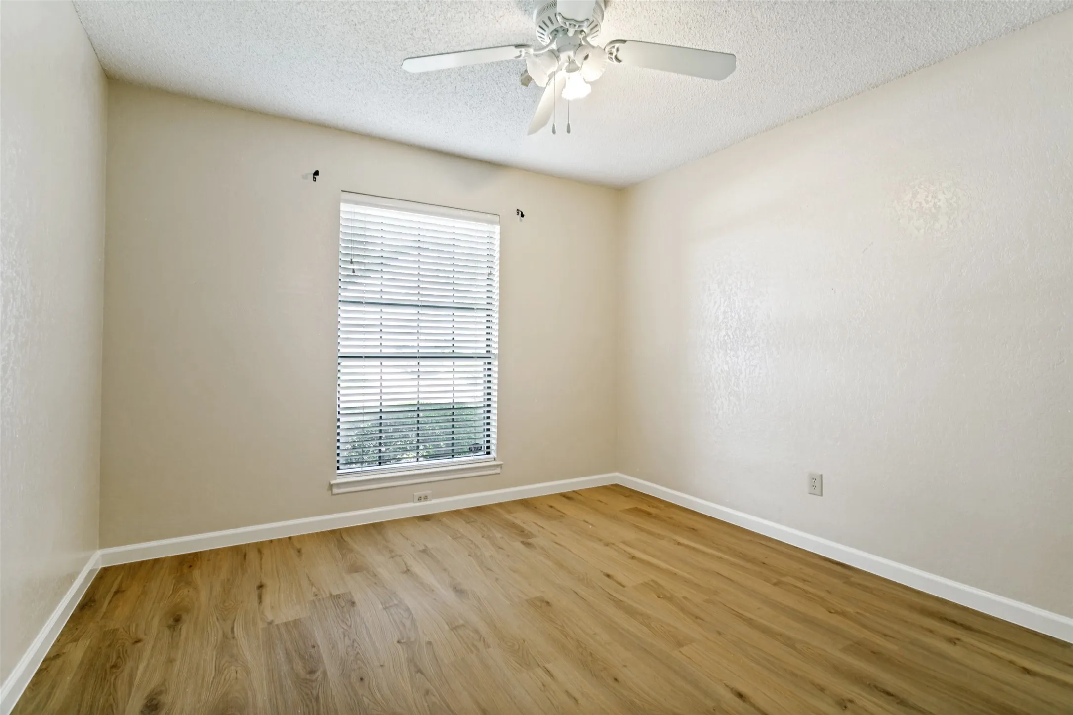 Room featuring wood-finish flooring, a window with blinds, a ceiling fan, and textured walls
