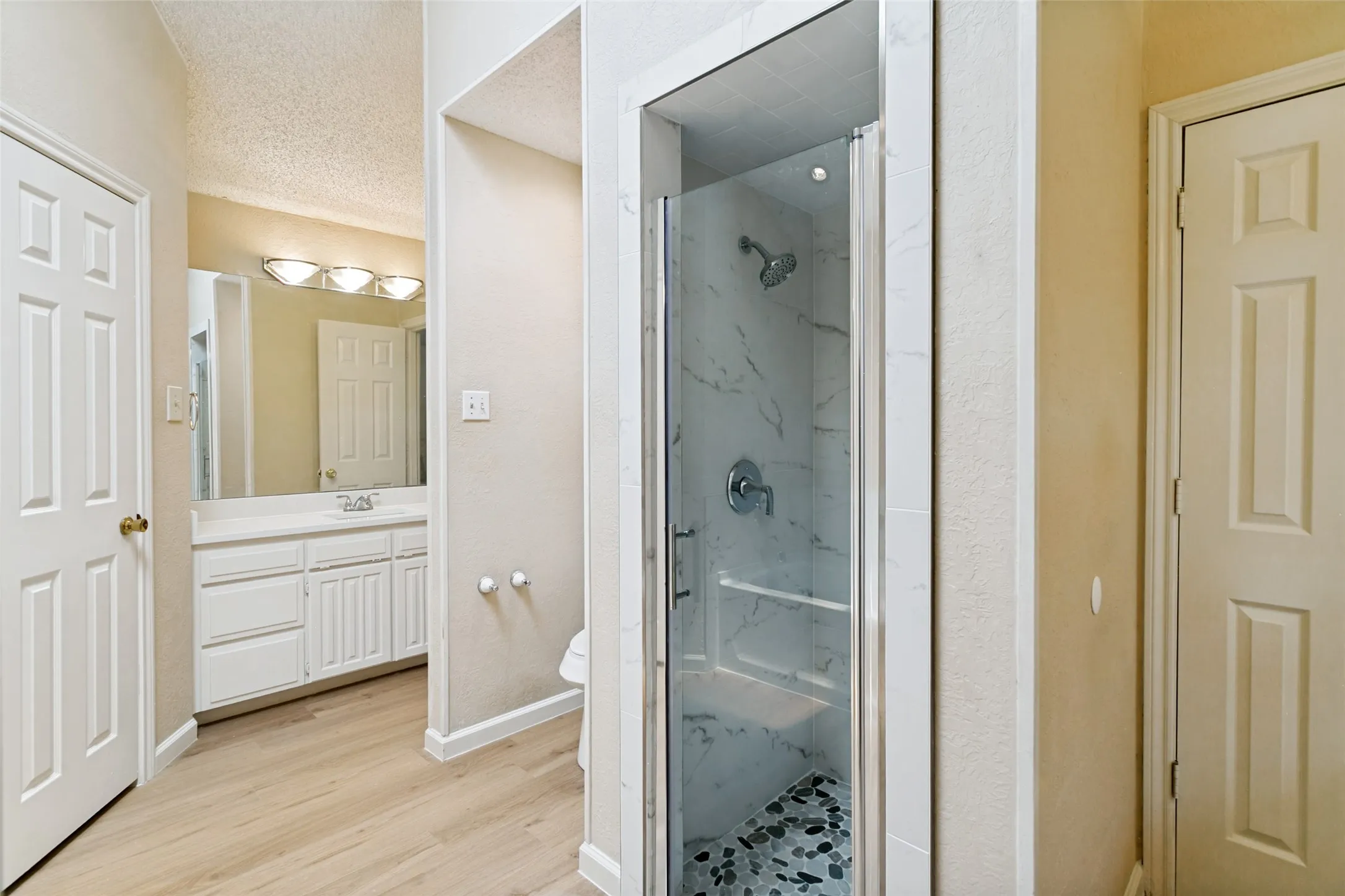 Contemporary bathroom featuring a glass-enclosed shower with pebble-tile flooring and marble-look wall tiling