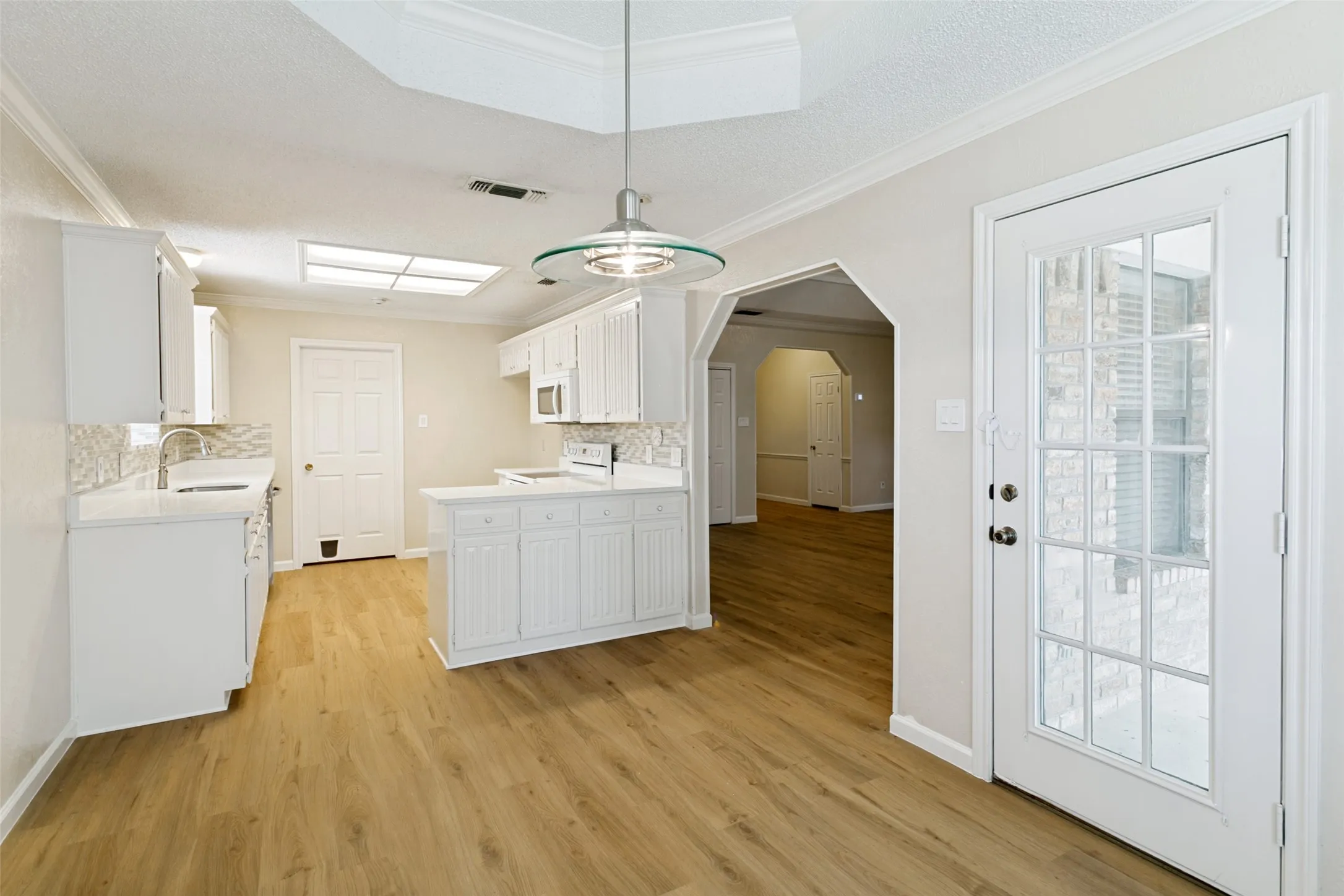 Open-concept kitchen with wood-finish flooring, white cabinetry, a built-in microwave, and a glass-paneled exterior door