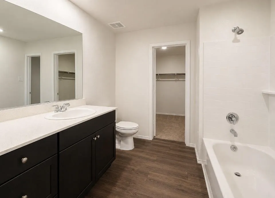 Full bathroom featuring a dark wood-finish vanity with a light-toned countertop, an integrated sink with chrome fixtures, a full-width mirror, and a bathtub with white subway tile surround and chrome showerhead