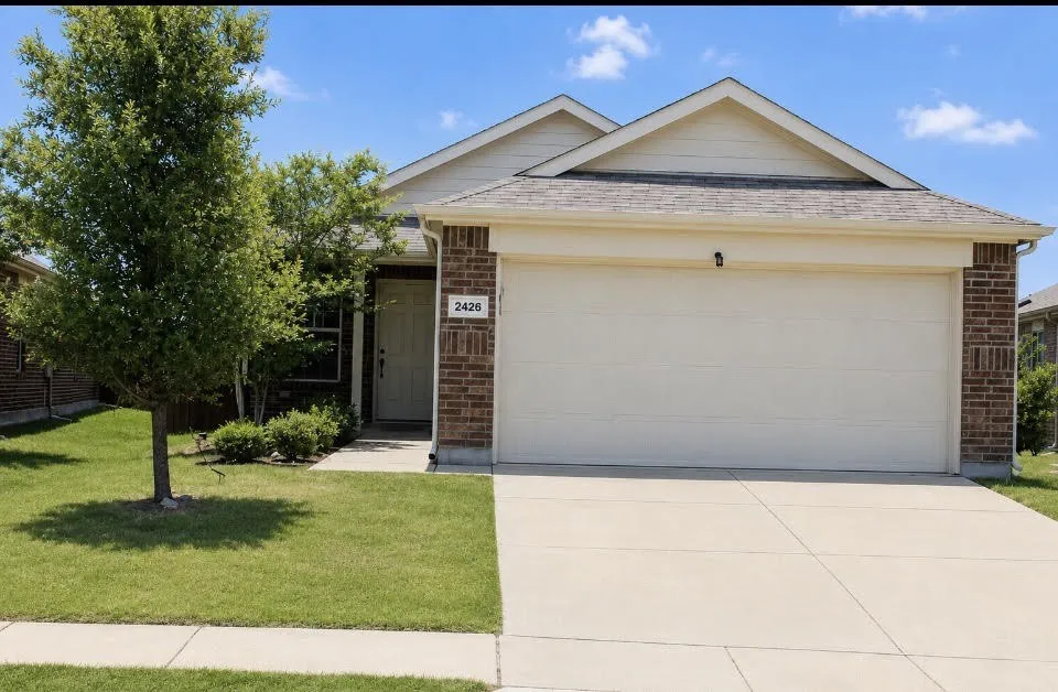 Front exterior featuring a brick and siding facade, a two-car garage, a concrete driveway, a manicured lawn, and mature trees