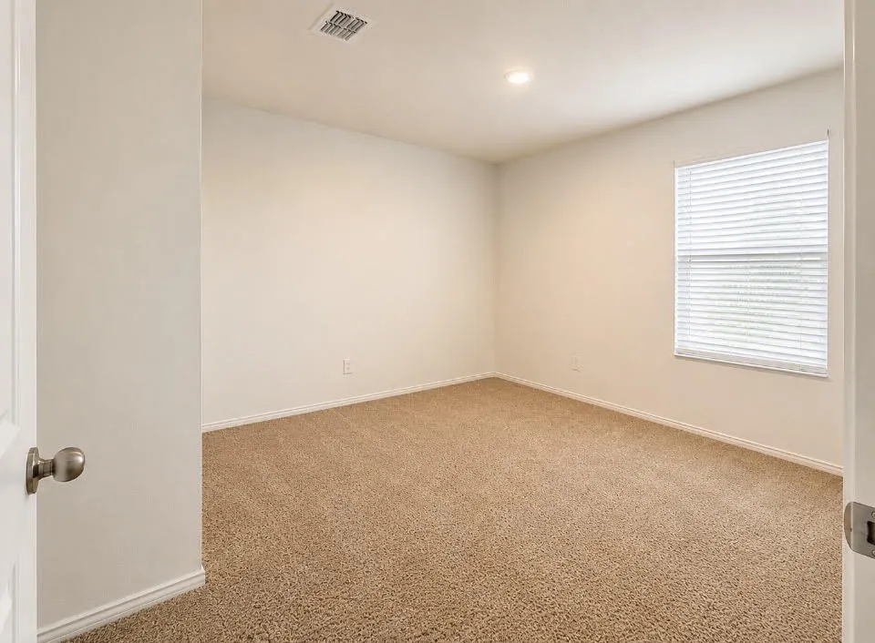 Carpeted room featuring a single window with blinds, recessed ceiling lighting, and a white door with a brushed nickel knob