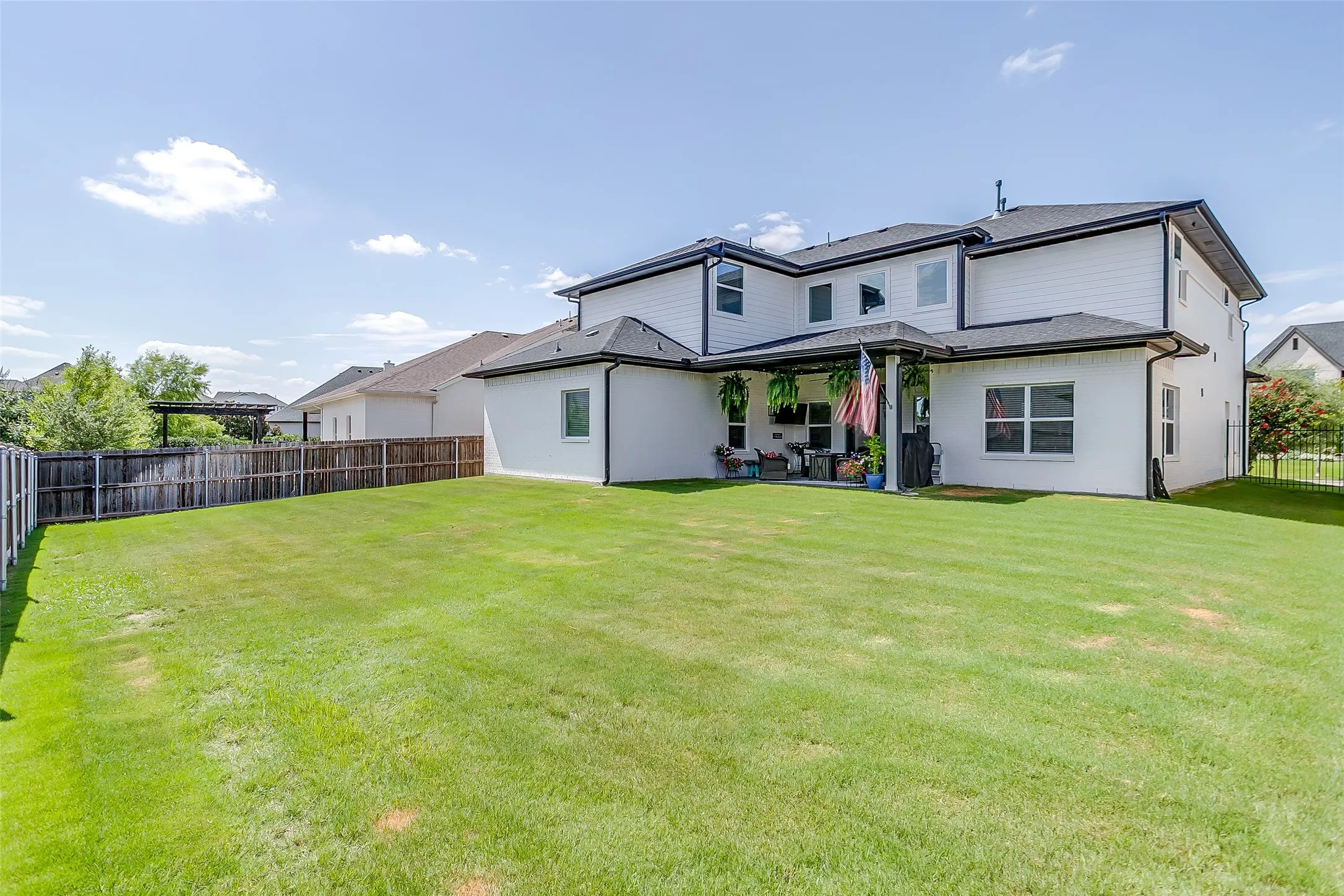 Expansive backyard featuring a manicured lawn, a full wooden privacy fence, and a covered patio with recessed lighting and a ceiling fan
