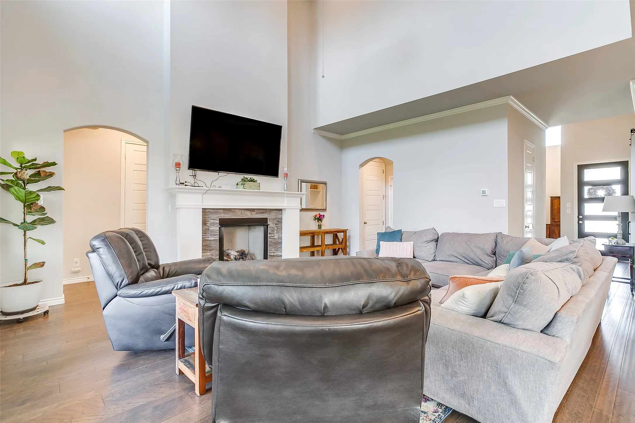 Living area featuring high ceilings, wood-finish flooring, a fireplace with stone surround and a white mantle, and an arched doorway