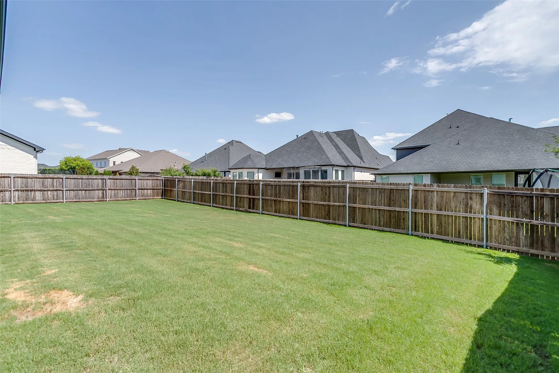 Expansive backyard featuring a large green lawn, full wood privacy fencing, and ample open space