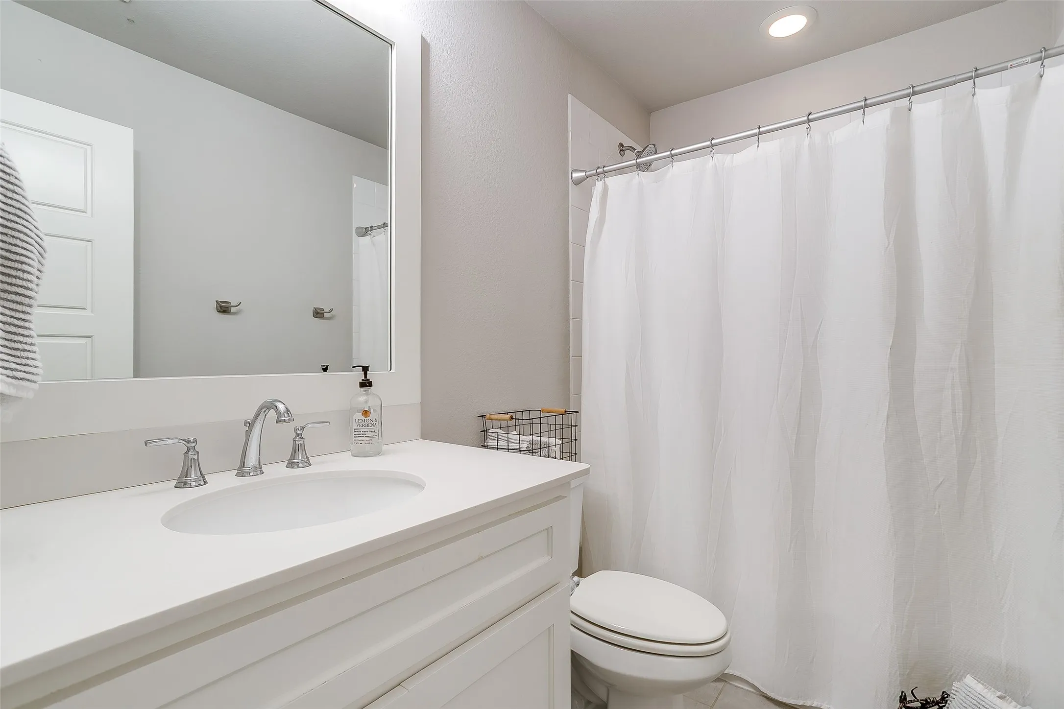Bathroom featuring a white vanity with an integrated sink and chrome faucet, a large framed mirror, a built-in toilet, and a shower with a white curtain