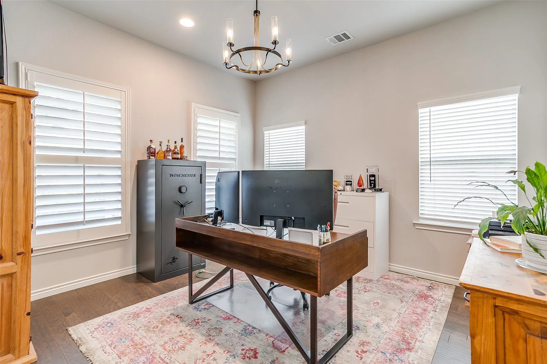 Room featuring wood-finish flooring, multiple windows with white plantation shutters and blinds, and a contemporary chandelier