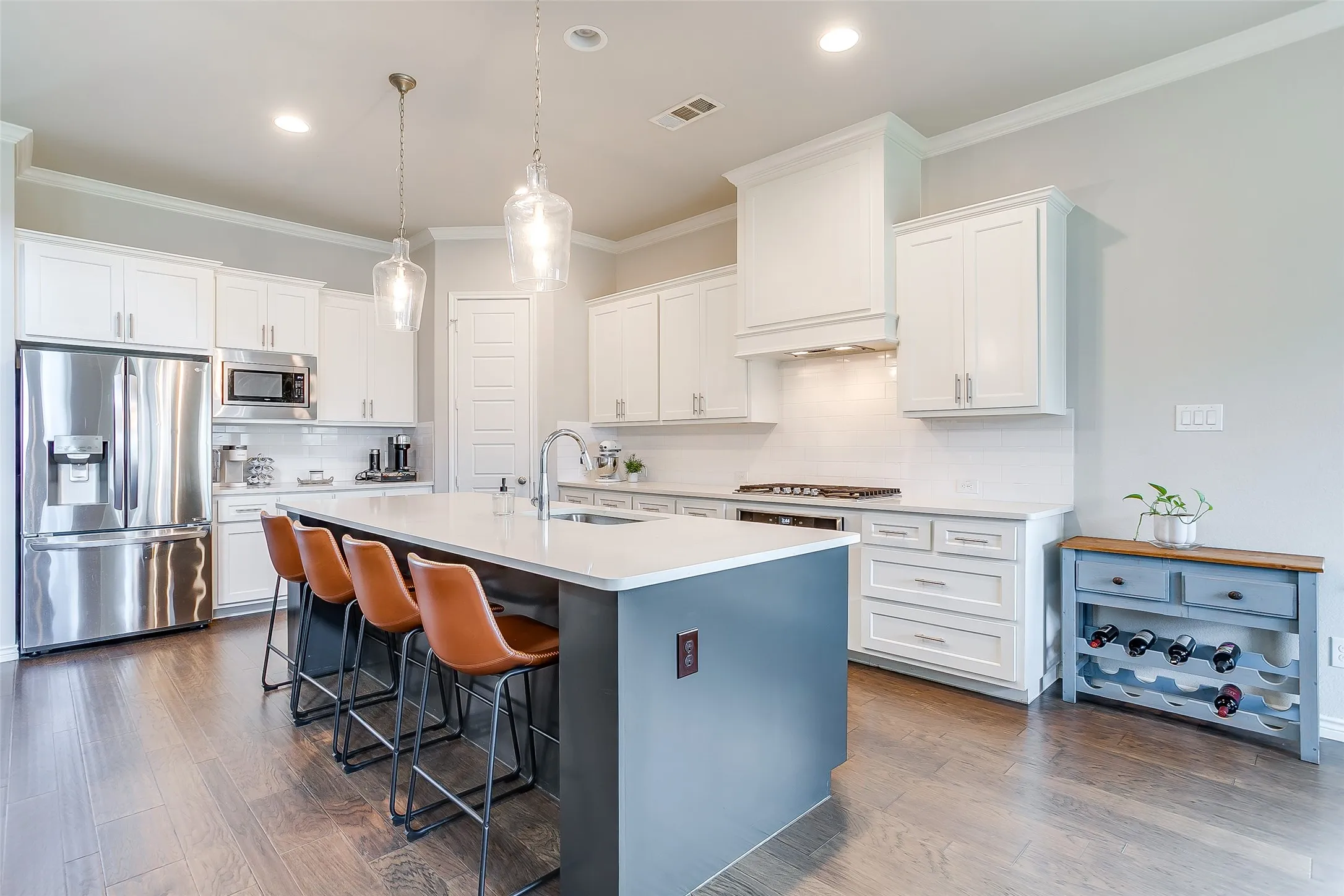 Gourmet kitchen featuring a large central island with seating, stainless steel appliances, white cabinetry, and wood-finish flooring