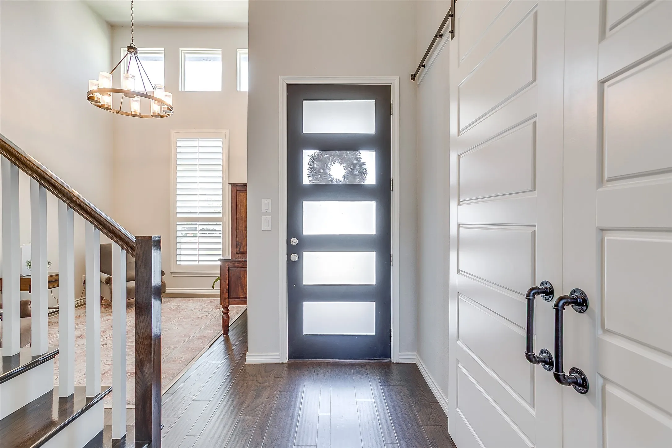 Entryway featuring dark wood-finish flooring, a modern black entry door with frosted glass panels, and a statement chandelier