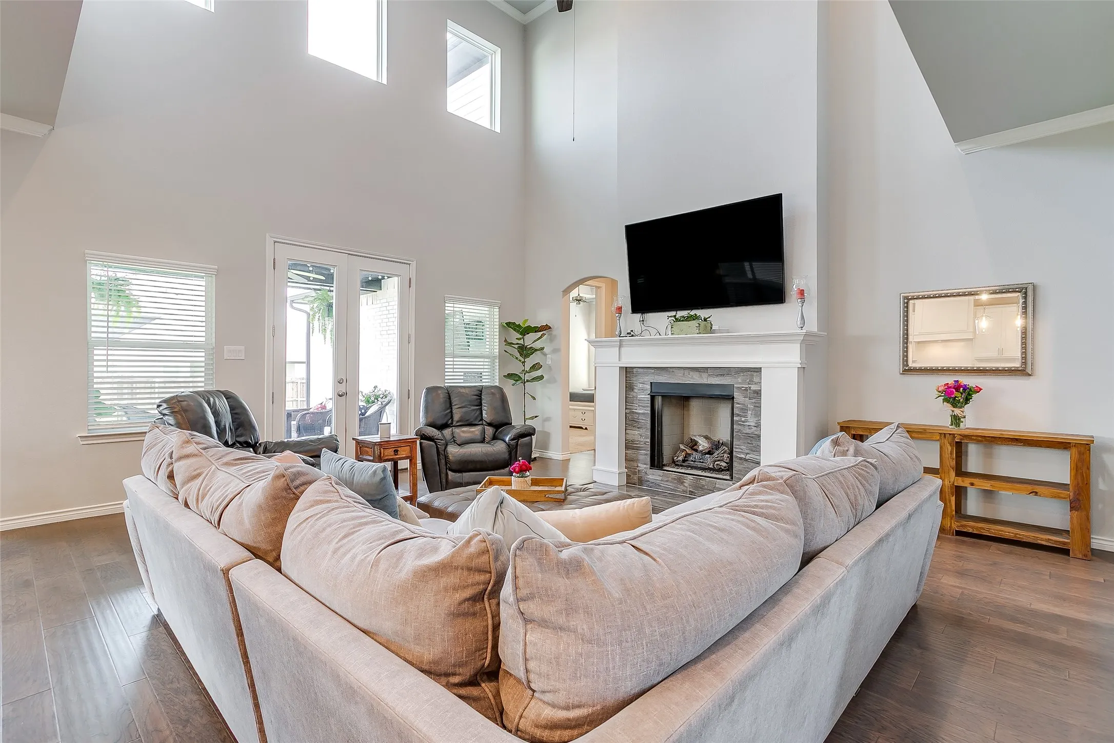 Living area featuring high ceilings, wood-finish flooring, a fireplace with a stone surround and white mantel, and double glass doors opening to an exterior space